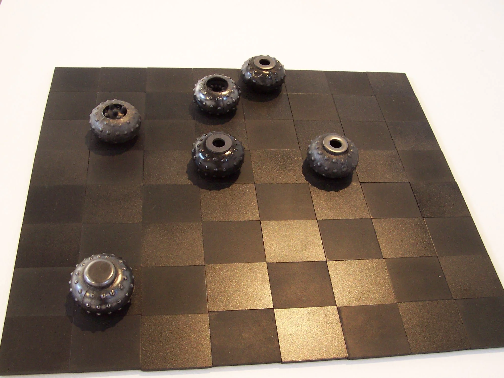 Objects resembling small, black, textured metal balls with holes in the center, arranged on a black grid surface.