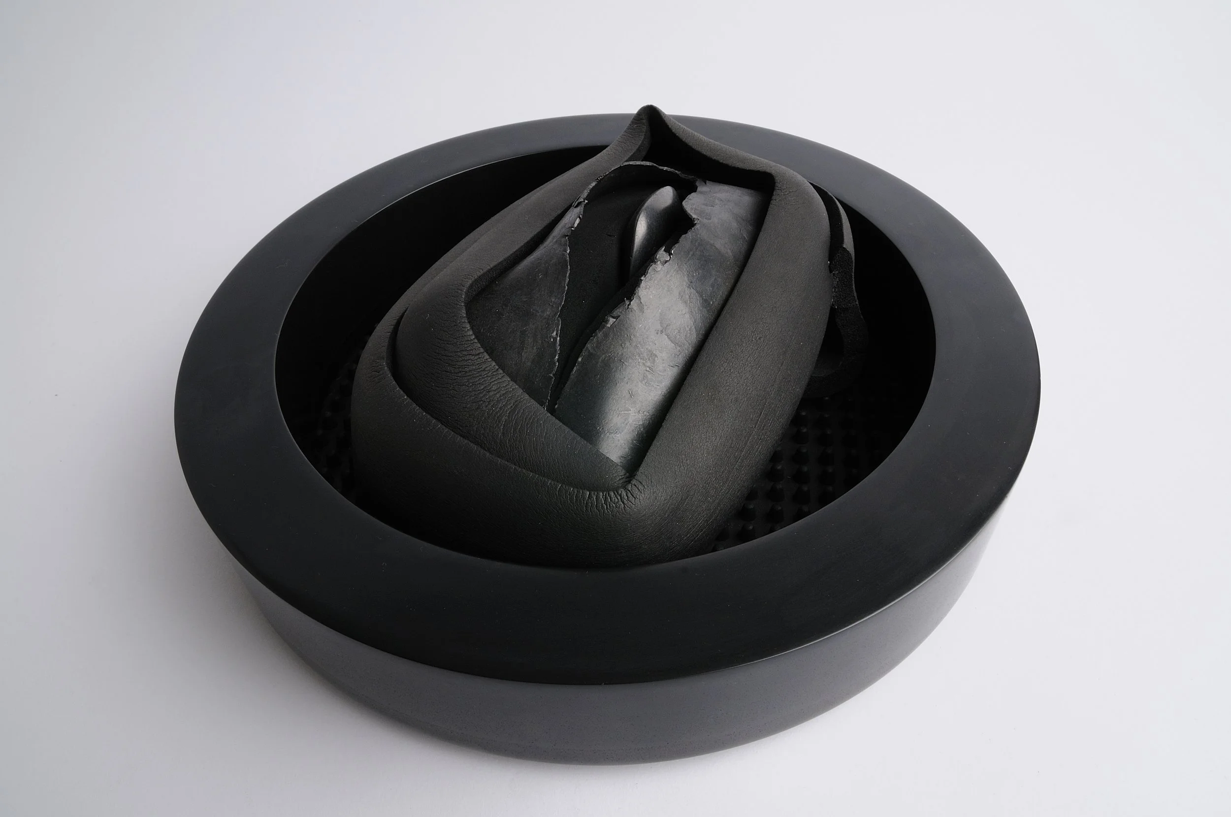 A black leather shoe inside a black circular container, with part of the shoe appearing damaged or peeled.