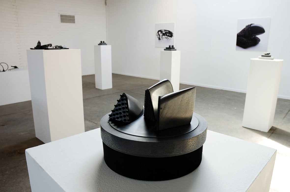 Contemporary art gallery displaying abstract sculptures on white pedestals, including a central geometric piece with curved black forms.