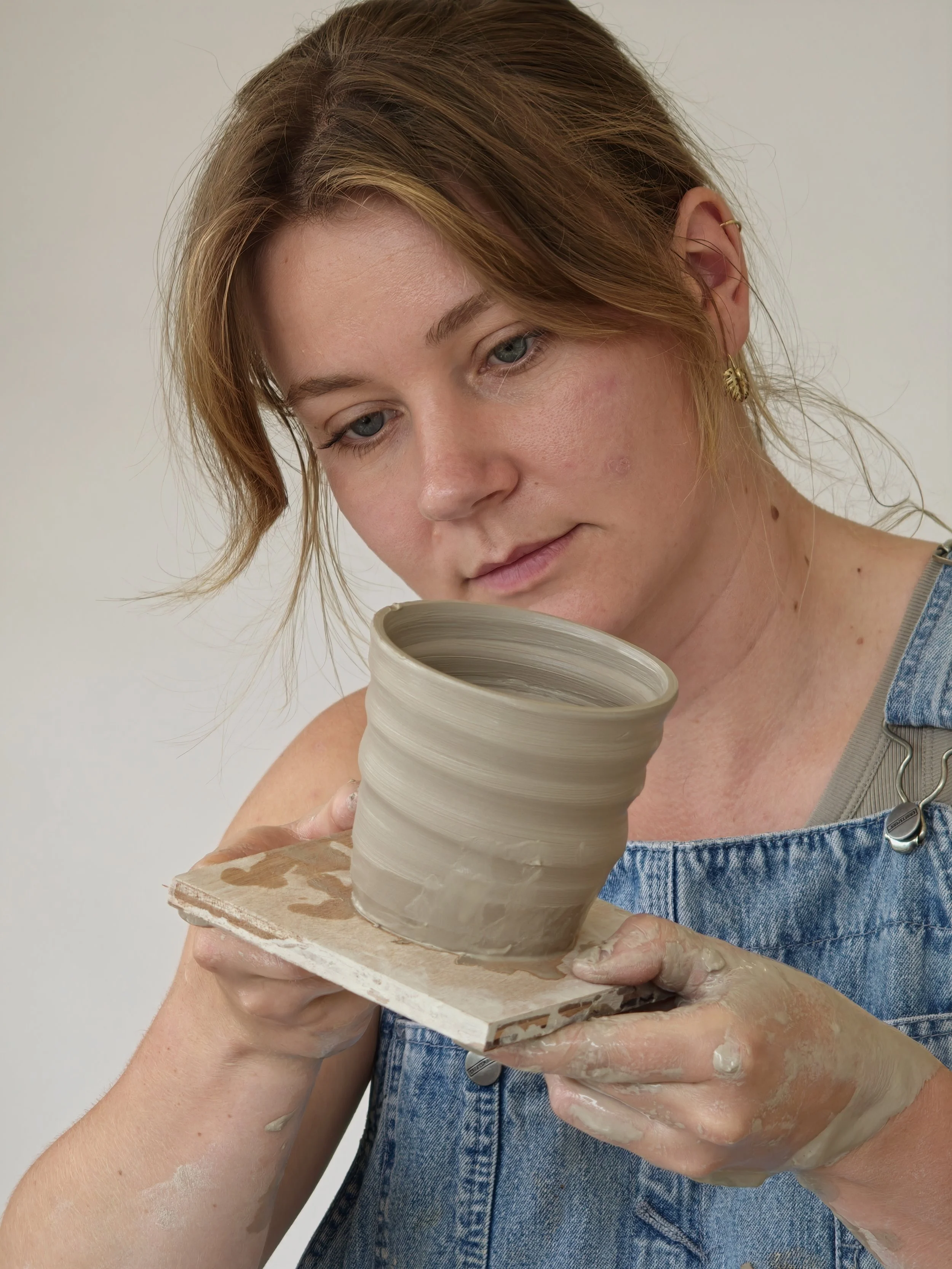 Vrouw die pottenbakken maakt met klei, terwijl ze haar handen en kleding bedekt met klei.