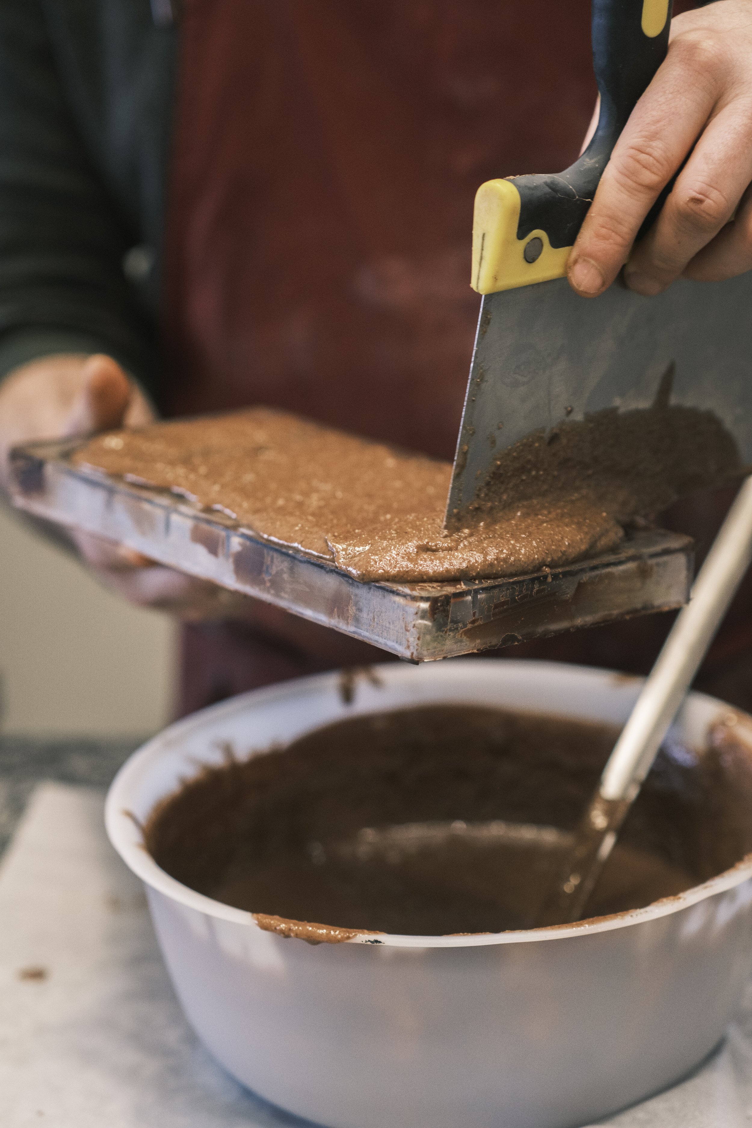 Personnes préparant du chocolat, avec une casserole de chocolat fondu sur la table et une plaque de chocolat en cours de découpage. | QSphotography | Namur