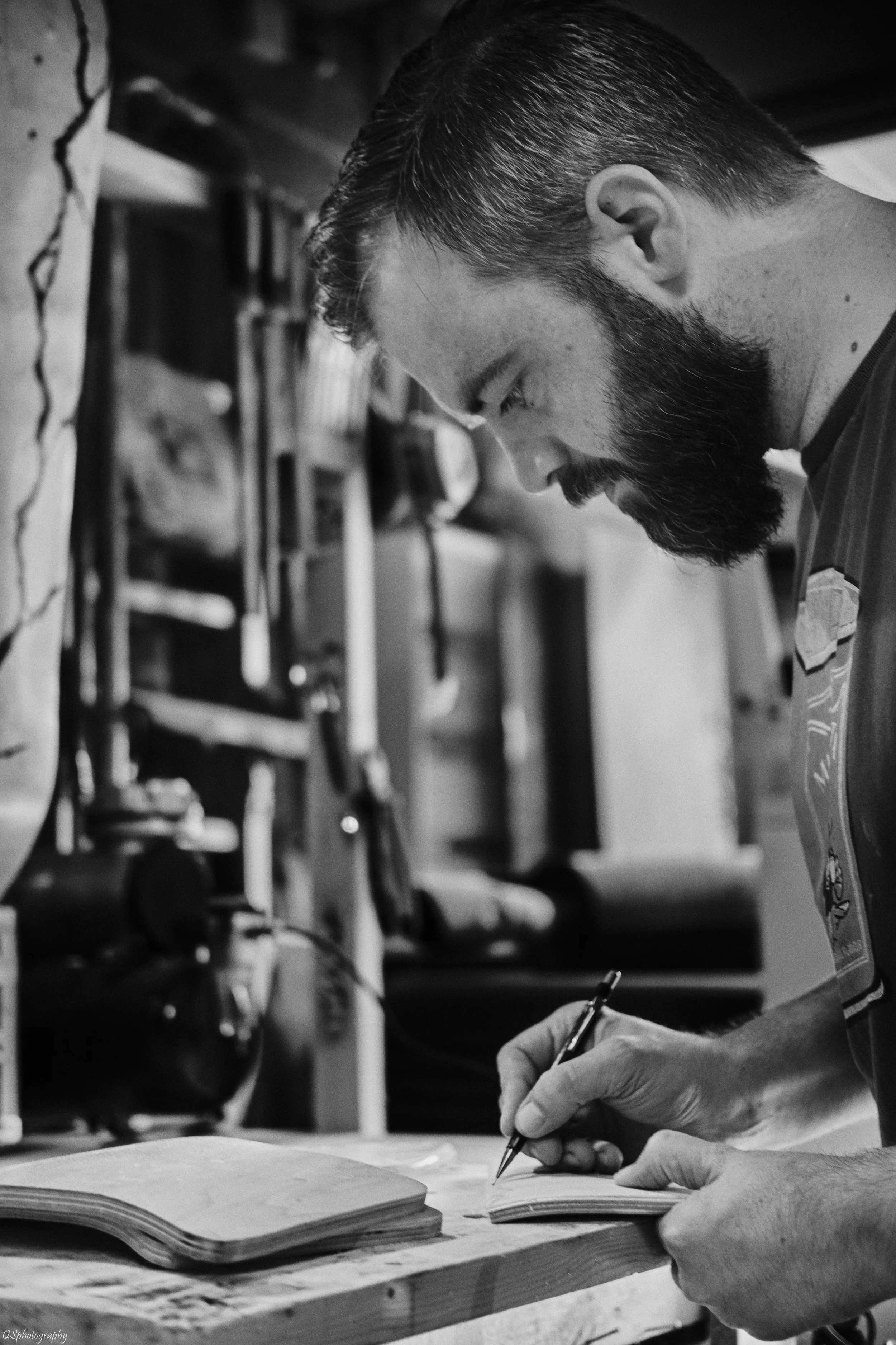 Un homme avec une barbe, concentré, écrit dans un carnet dans un atelier. | QSphotography | Namur