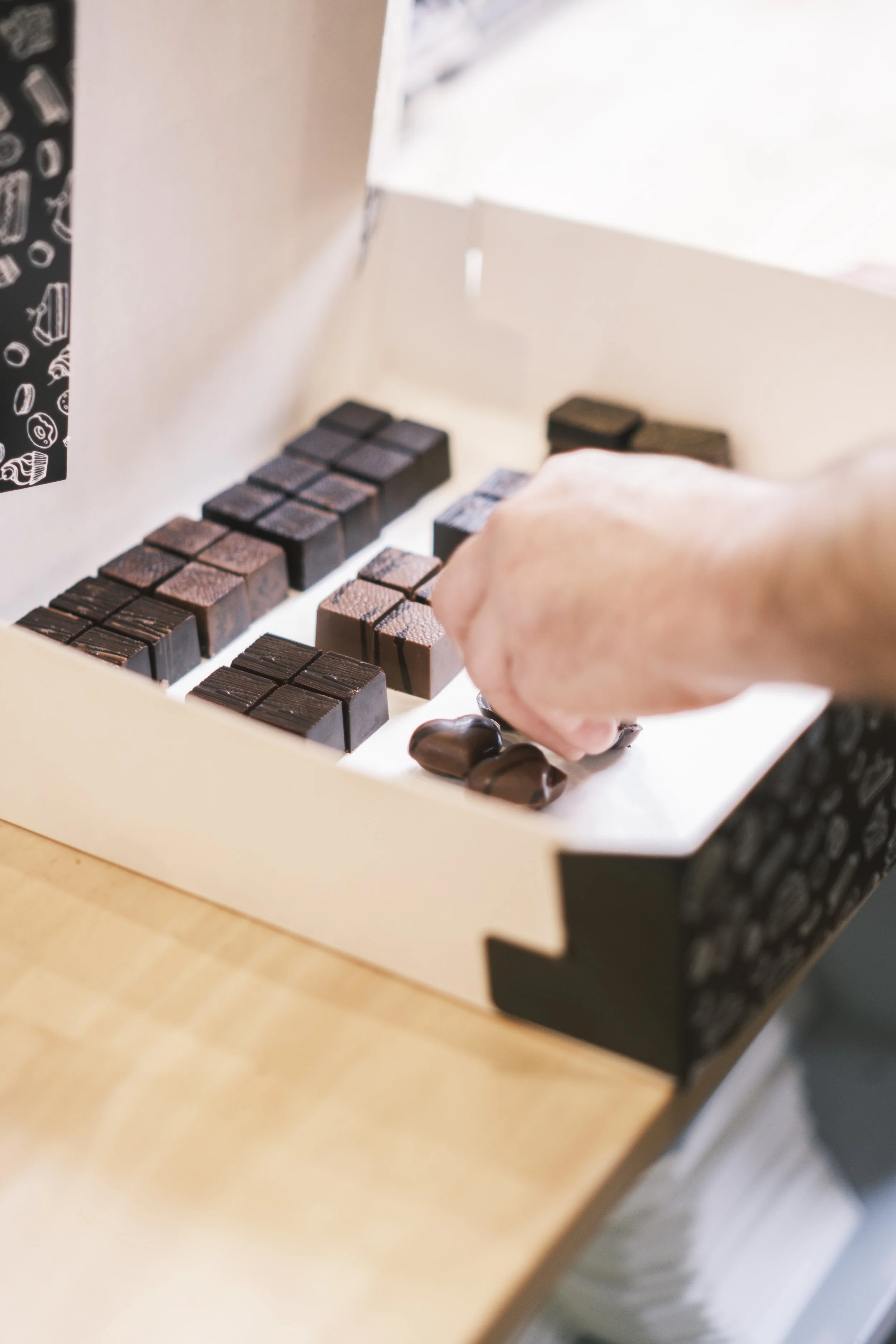 Une main sélectionnant des chocolats dans une boîte contenant divers types de chocolats. | QSphotography | Namur