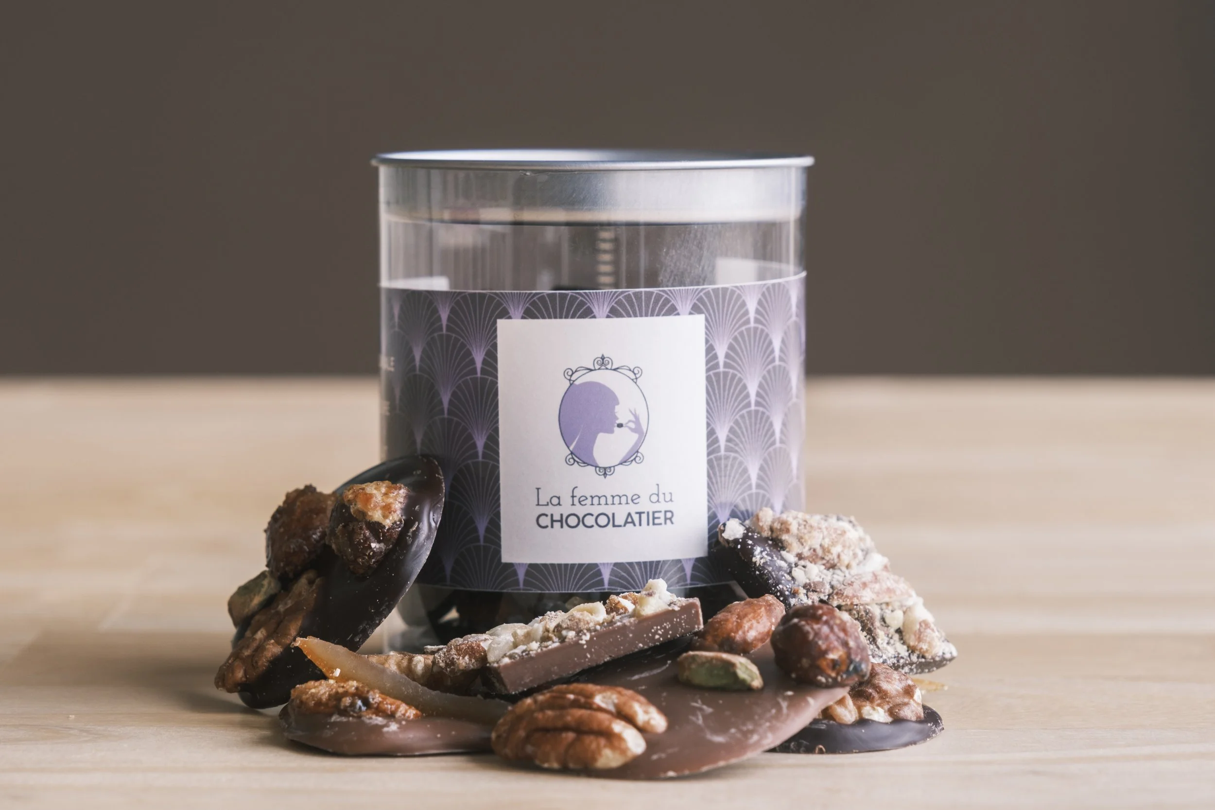 Un assortiment de chocolats avec un contenant portant le logo 'La femme du Chocolatier' sur une table en bois.  | QSphotography | Namur