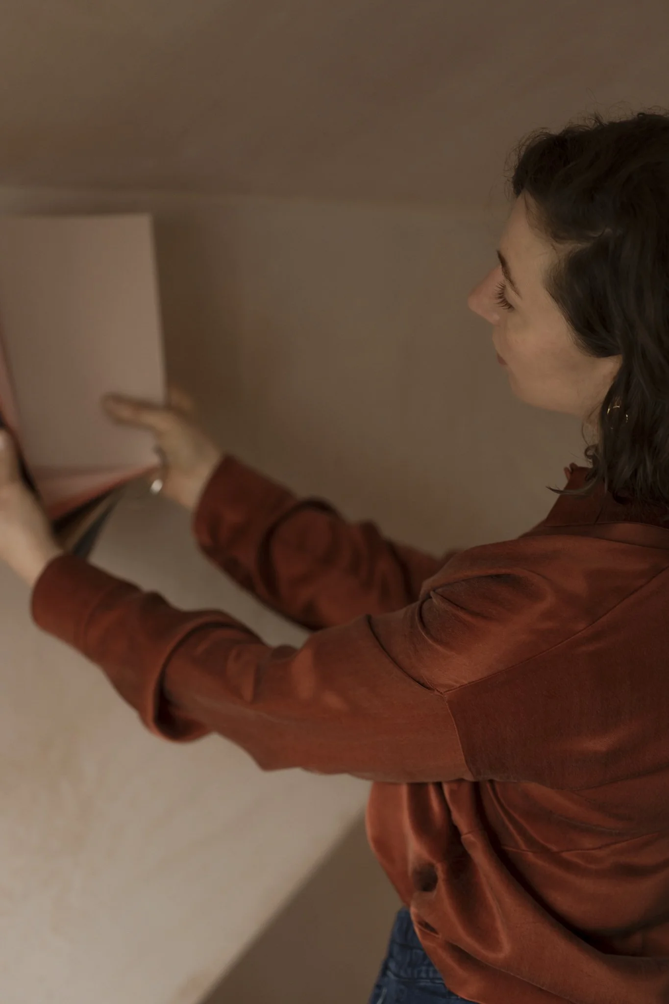 A woman with curly brown hair wearing an orange blouse looking at colour samples.