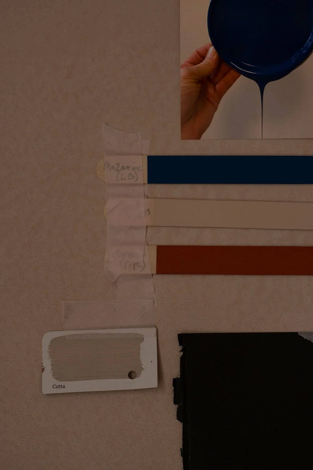 Colour swatches labeled 'Cotta', 'Mazarine (LG)', and other labels, with a hand holding a blue paint container pouring paint, and a small note taped to the wall as a moodboard