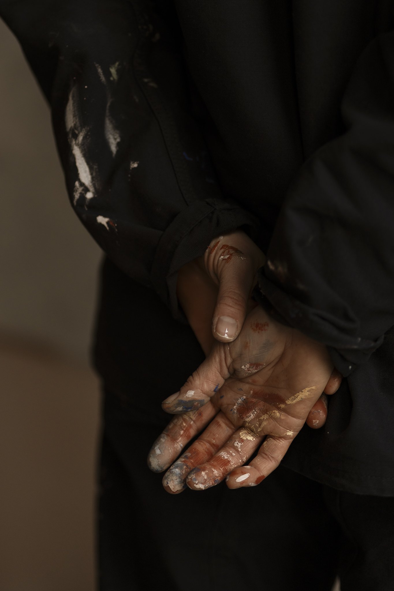 Close-up of hands covered in white paint, holding a paintbrush and painting on a person's leg, wearing black pants.