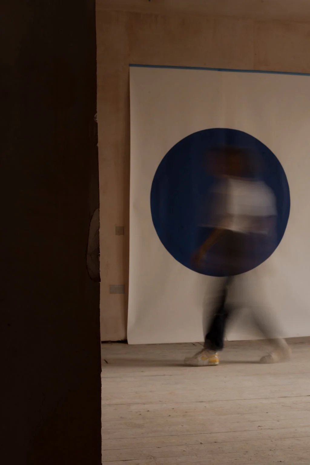 Blurred person walking past a large artwork with a dark blue circle on it.