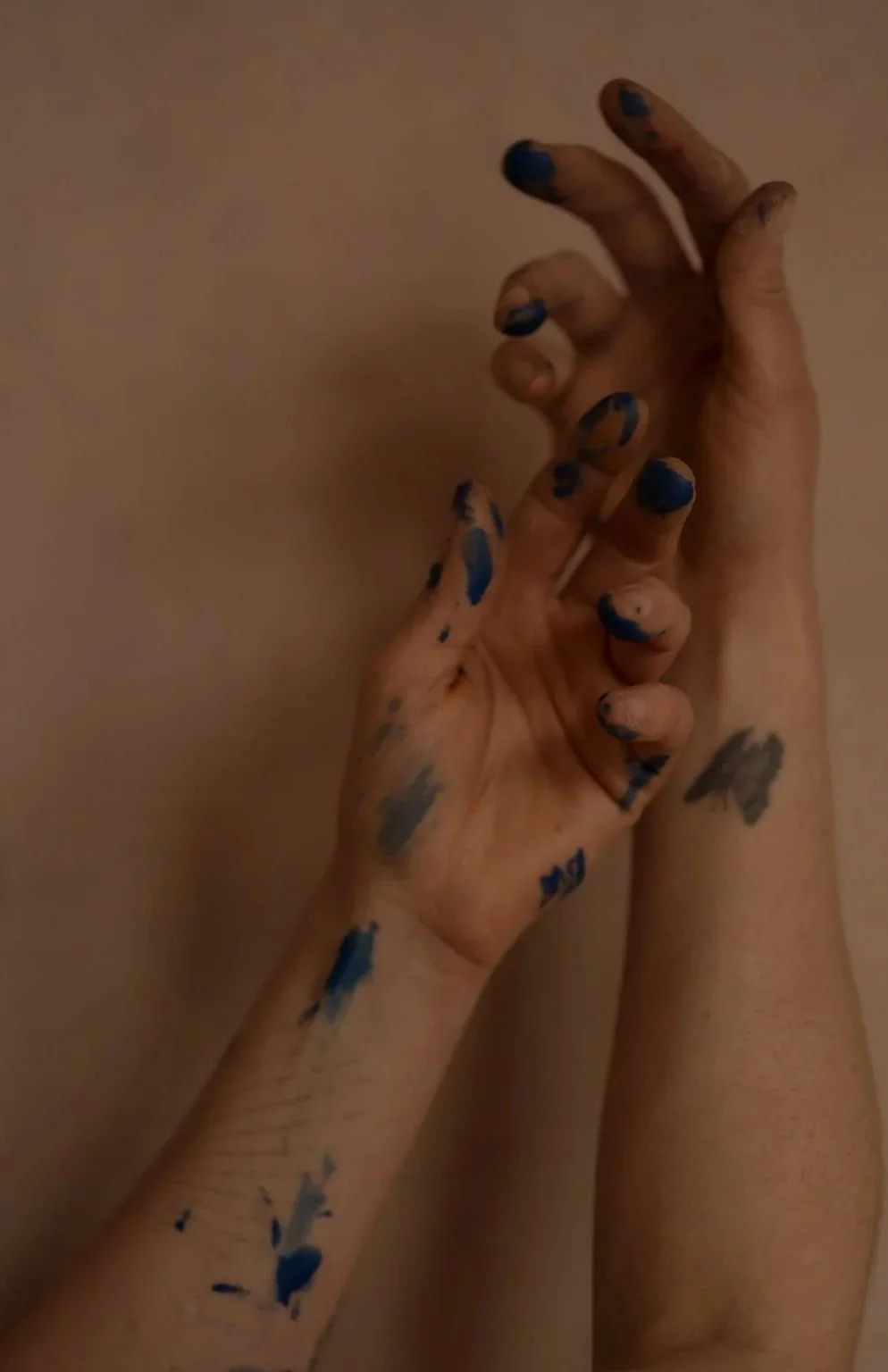 Two hands, one with blue and black paint, touching the other hand against a plaster background.