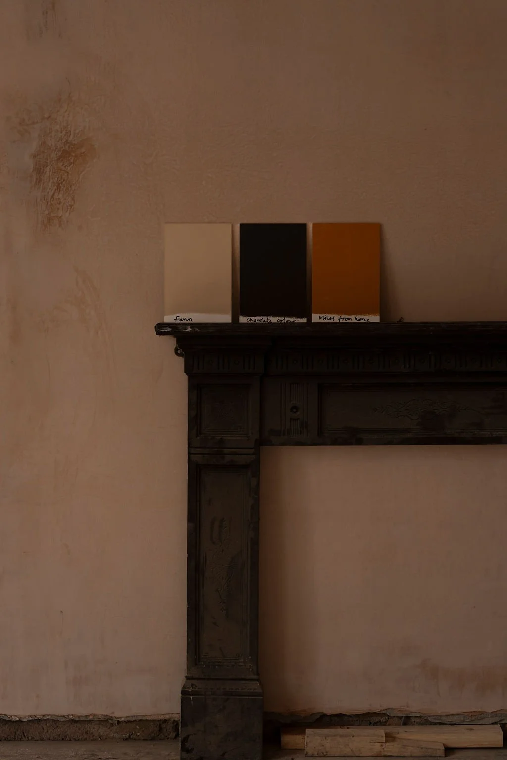 Three small colour swatches on top of a fireplace mantle against a plastered wall.