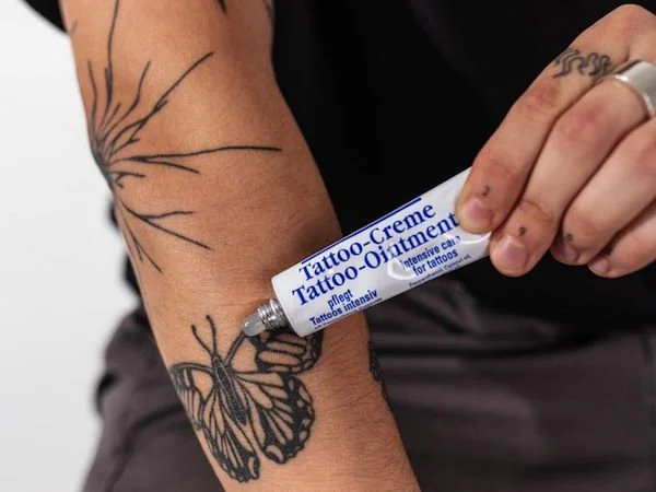 Person trägt Tattoo und benutzt eine Tube Tattoo-Creme auf dem Arm.
