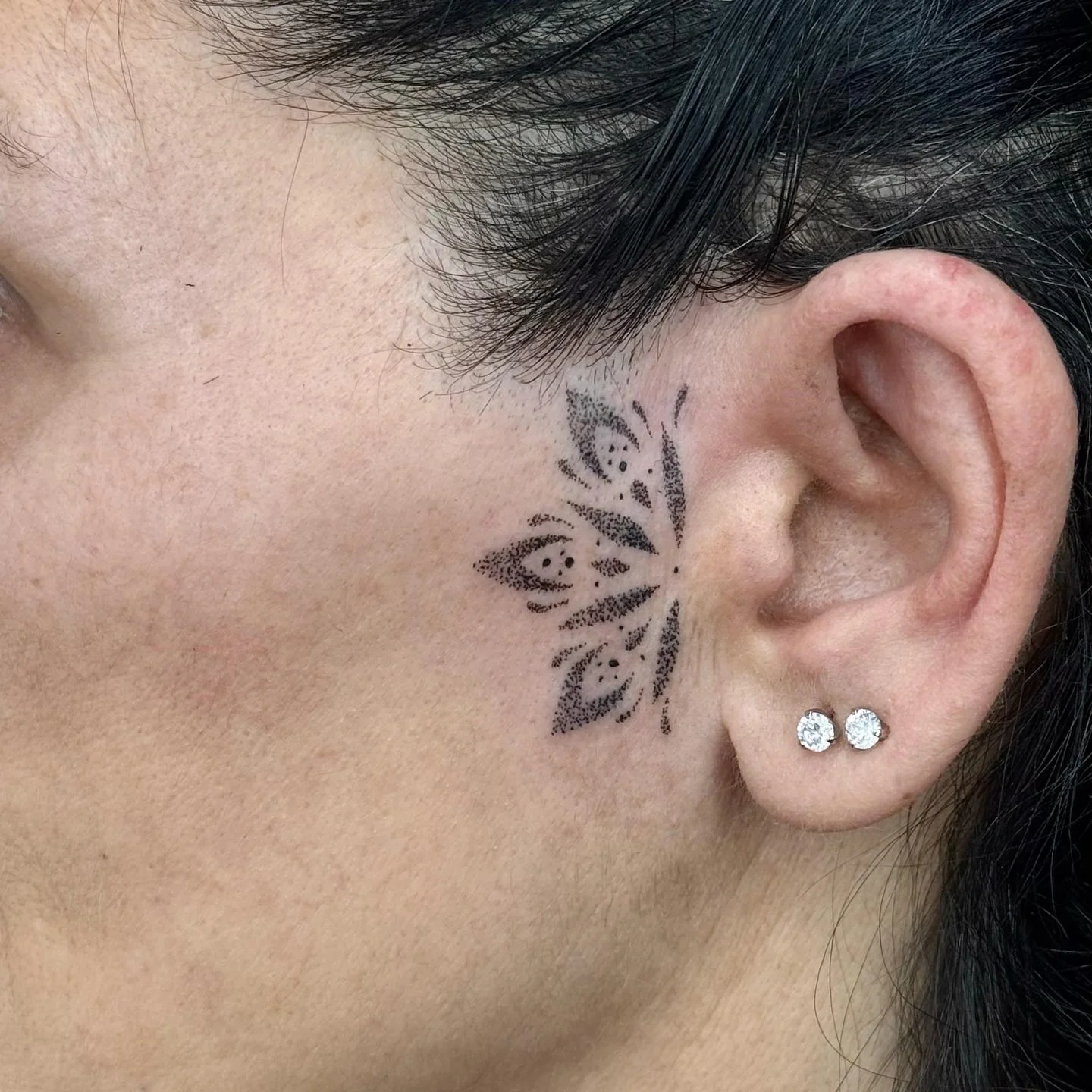 Nahaufnahme eines Ohrrings und eines Tattoos hinter dem Ohr, das wie ein Schmetterling aussieht.