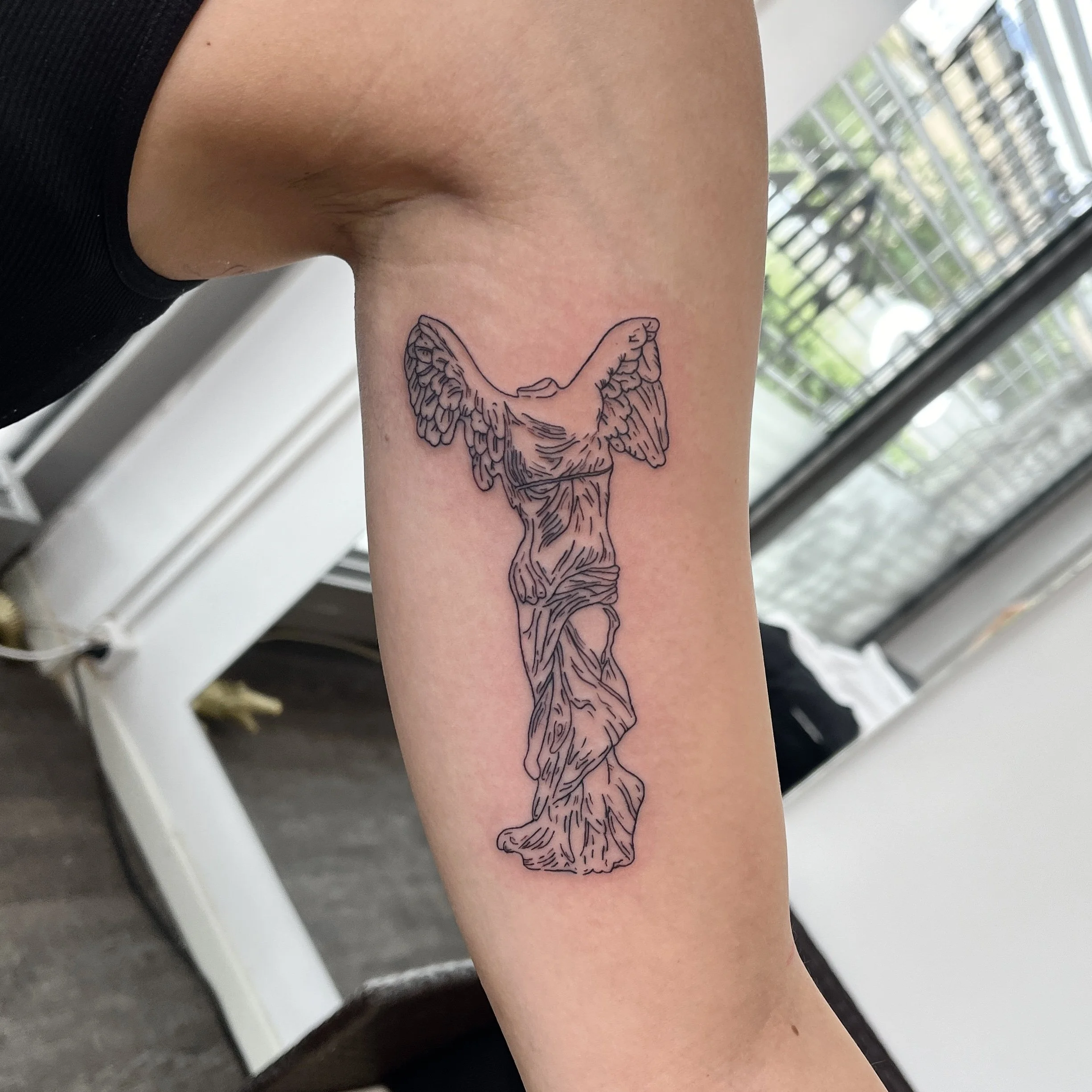 Tattoo einer stilisierten, skizzenhaften Darstellung der Skulptur Venus von Milo auf dem Oberarm.