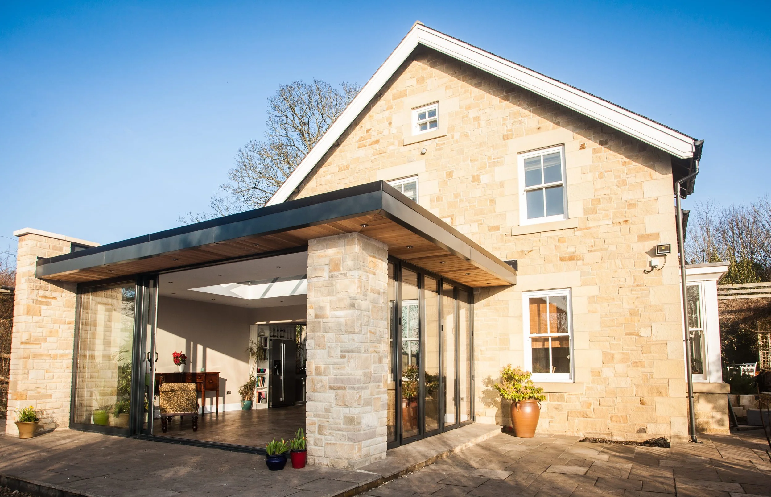 A modern house with a stone exterior and a glass-enclosed patio area, featuring sliding doors and potted plants outside.