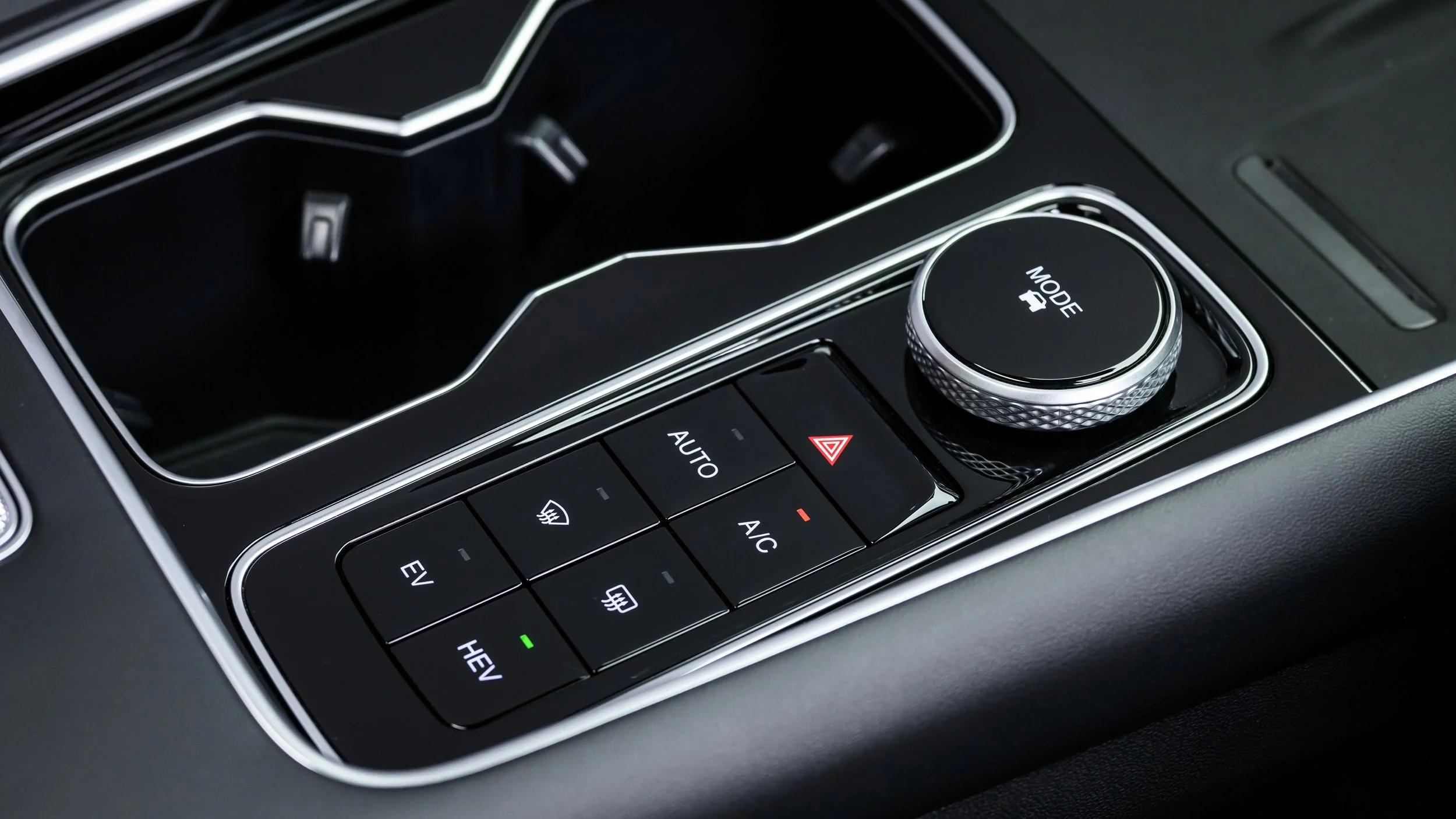 Close-up of a car's center console with climate control buttons, rotary mode selector, and a cup holder.