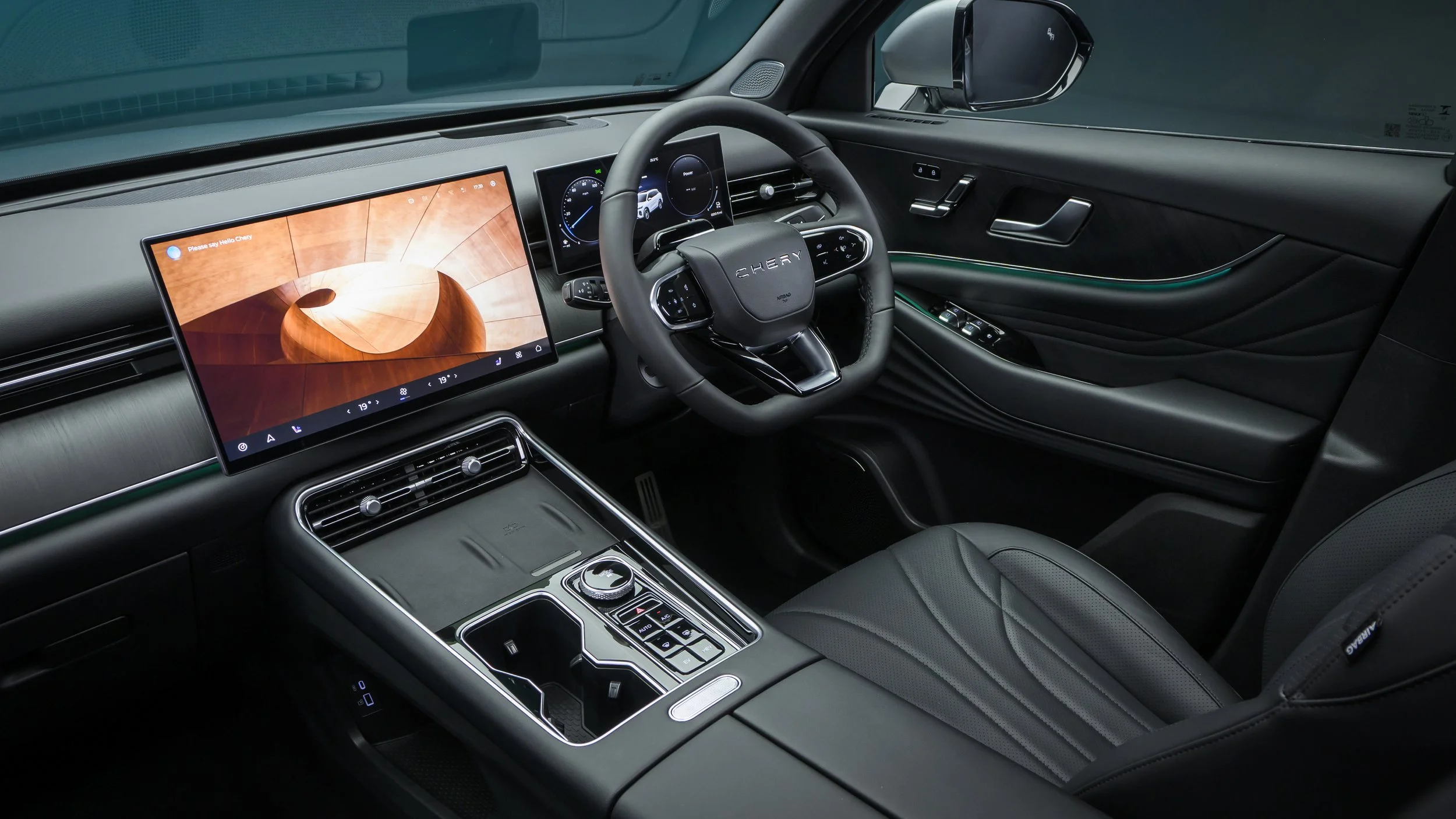 Interior of a modern vehicle showing a large digital display screen on the dashboard, a steering wheel with the brand name 'Chery', and various control buttons, all in a sleek black and modern design.
