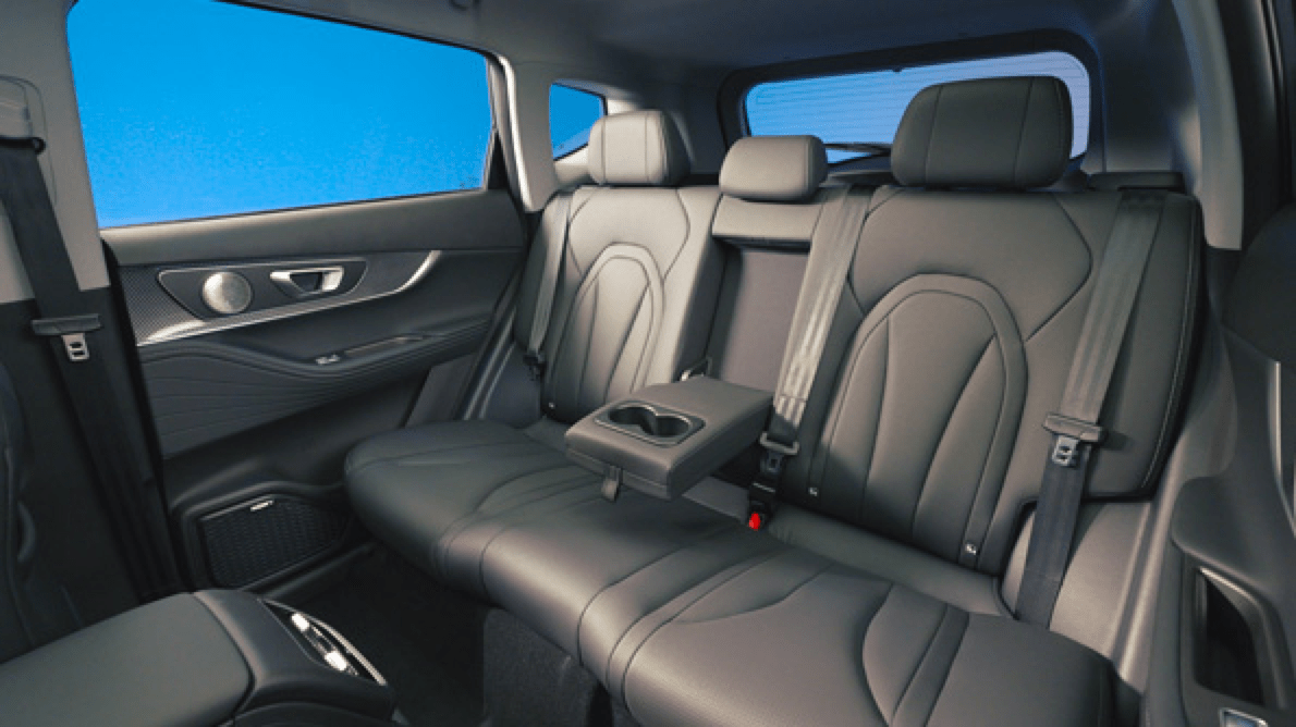 Interior of a luxury vehicle's back seat with black leather seats, three headrests, a fold-down center armrest with cup holders, and side windows with blue tint.