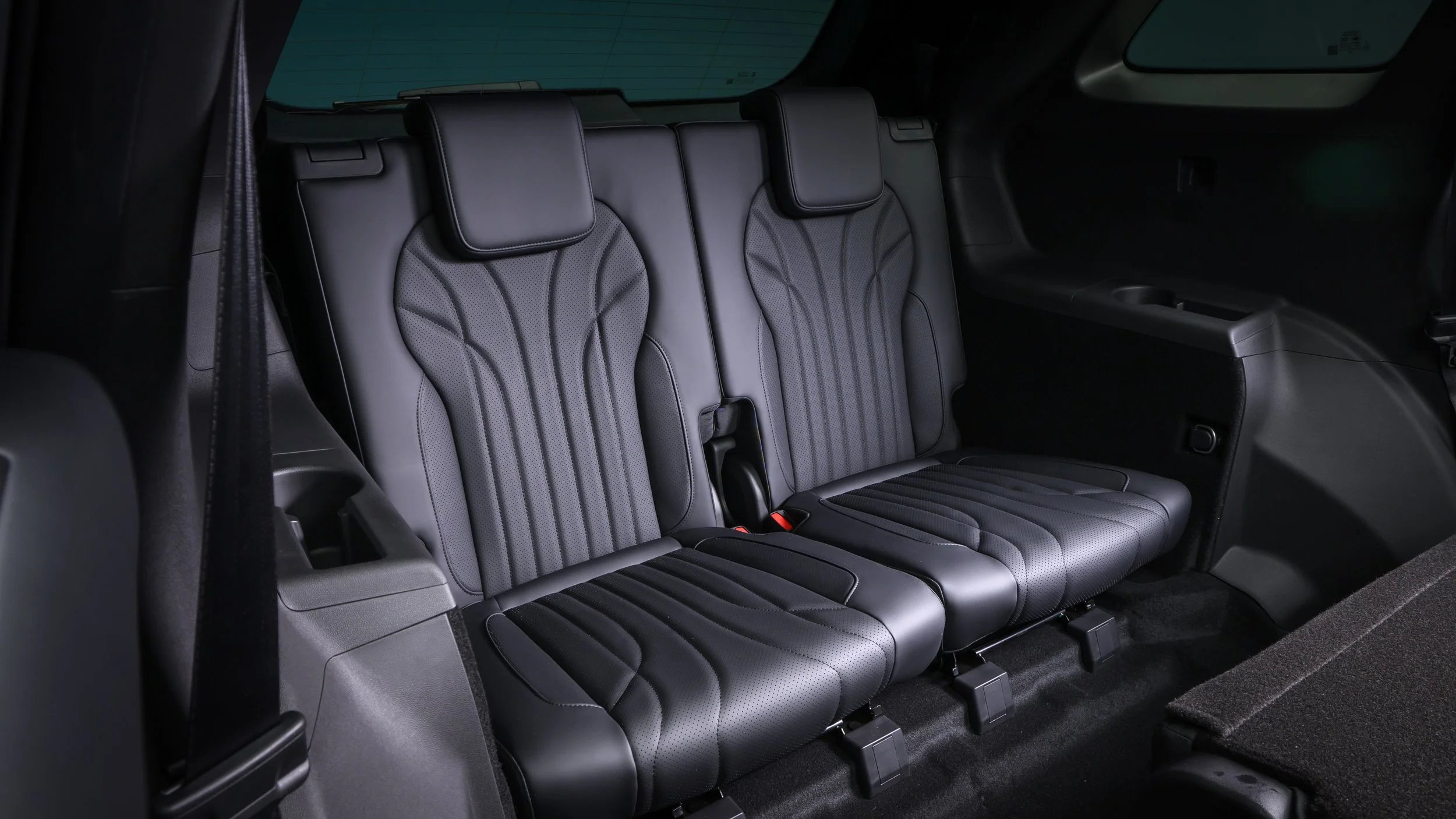 The backseat of a modern black SUV with three leather seats and headrests, interior lighting