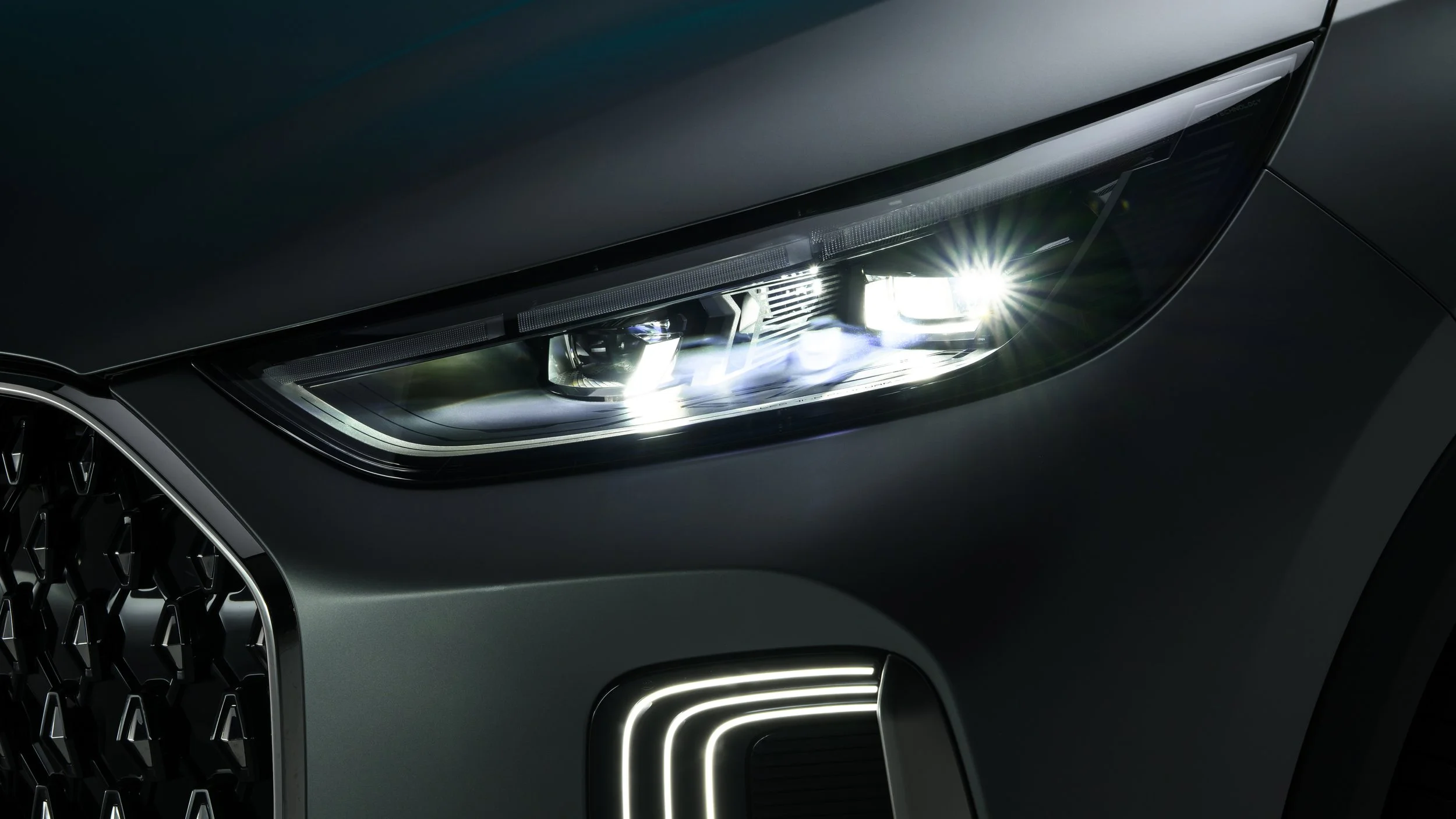 Close-up of a luxury car's front headlight and part of the grille, with sleek black and chrome detailing.