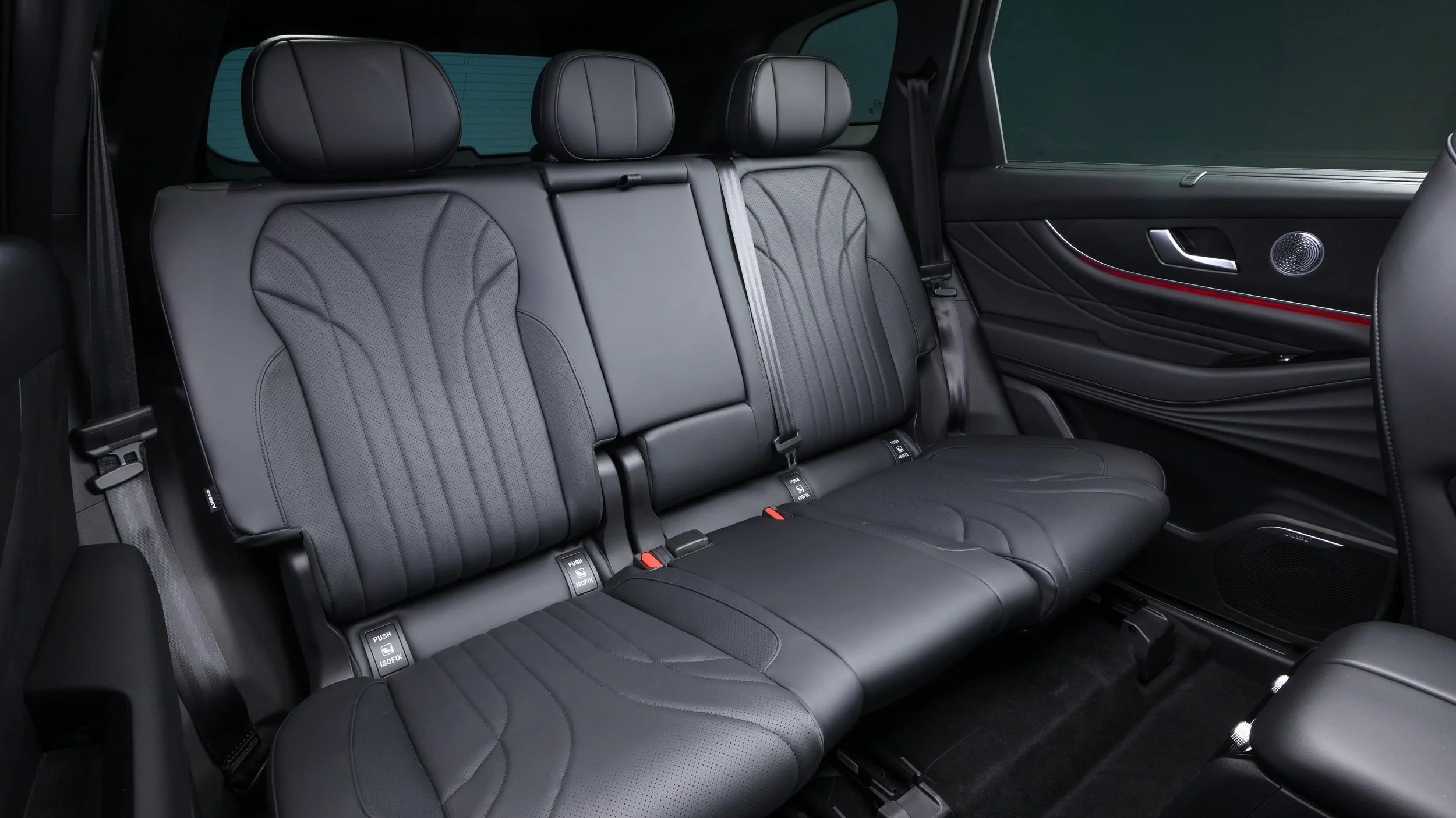 Black leather back seat of a car with three headrests and seatbelts.