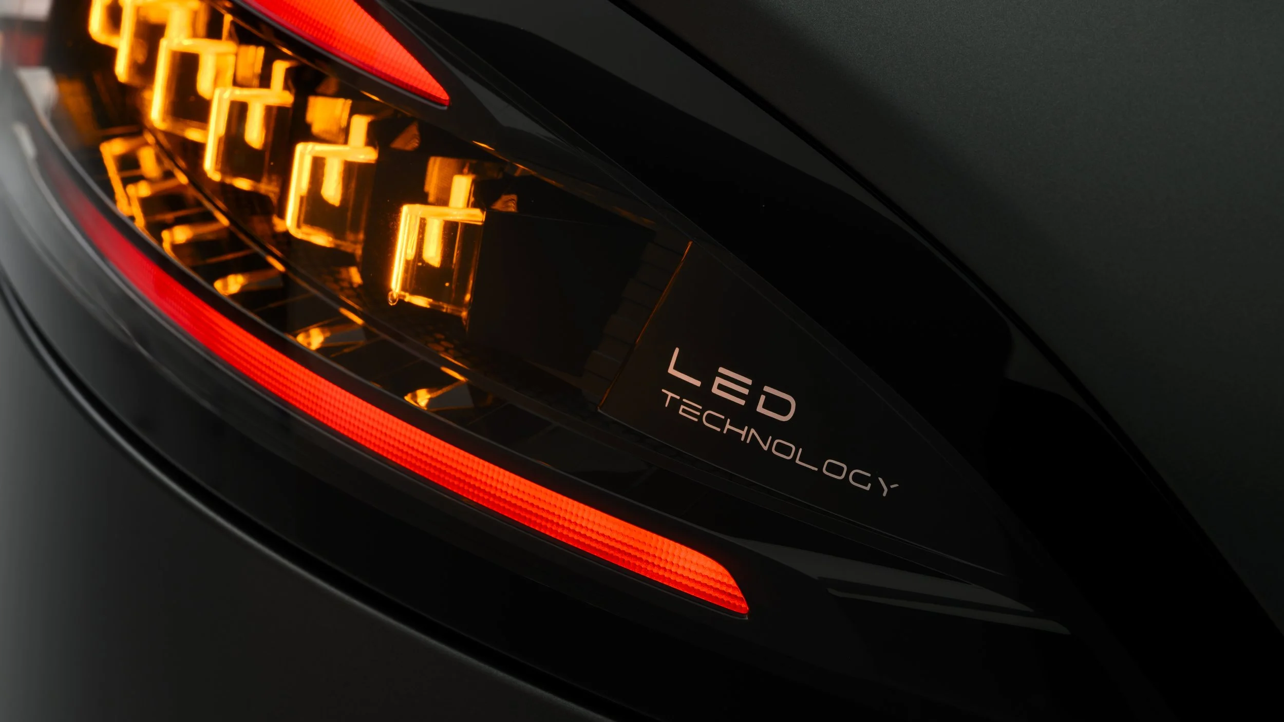 Close-up of a car's taillight showing a black surface with illuminated orange LED lights and the words 'LED TECHNOLOGY' on a black label.