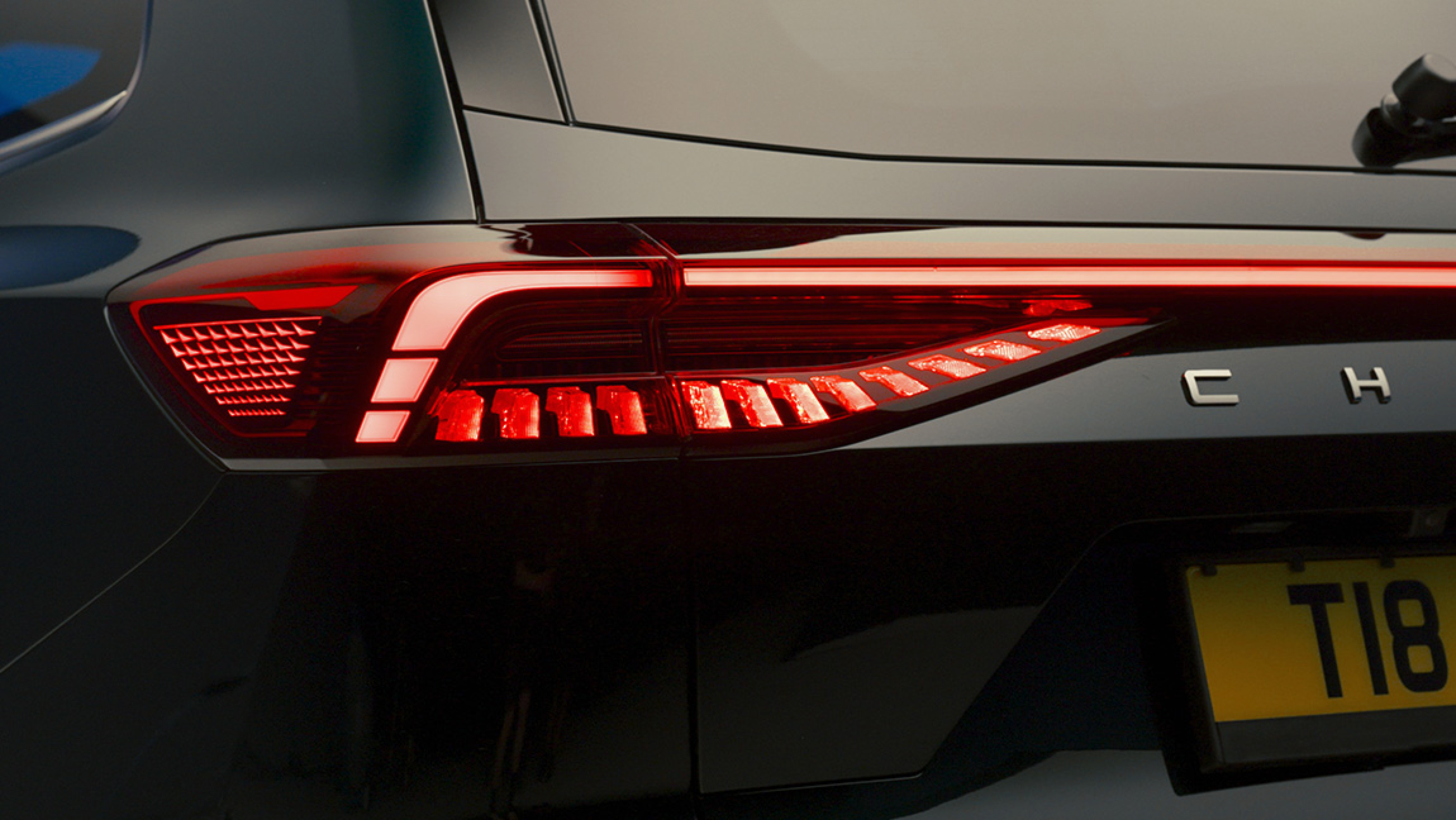 Close-up of the rear of a black modern luxury car, showing the tail light with red LED lights and the car's glossy surface reflecting ambient light.