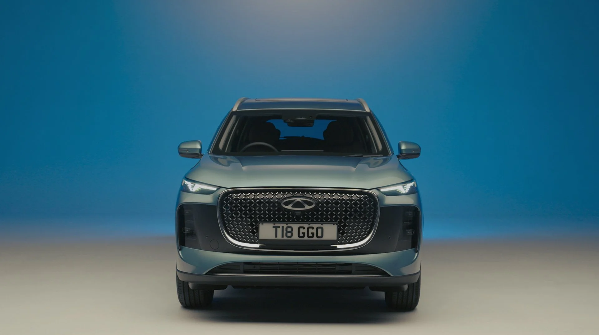 Front view of a gray compact SUV with a distinctive large black grille and slim headlights, parked against a gradient blue background.