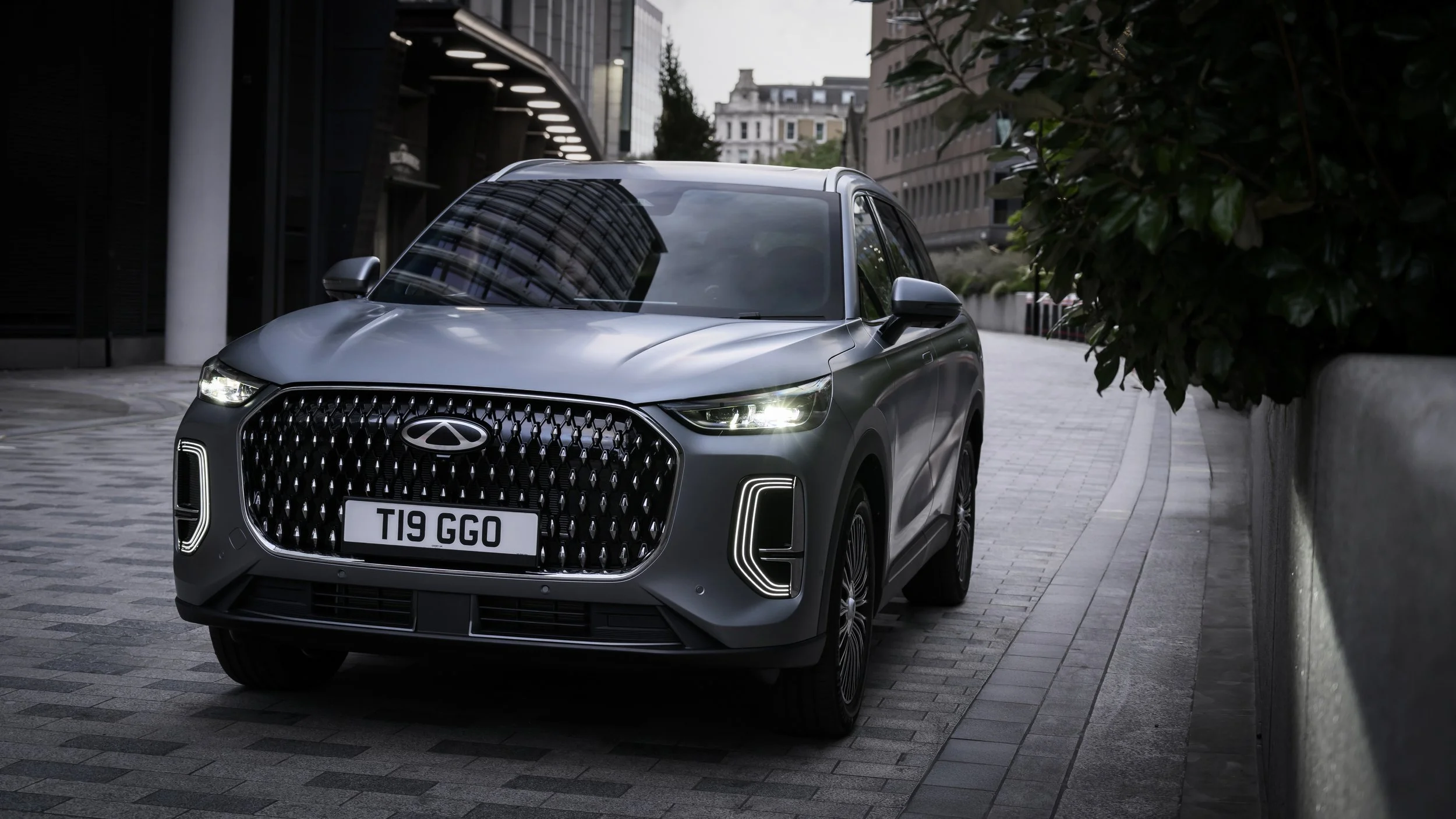 A gray SUV parked on a city street with modern buildings and greenery around.