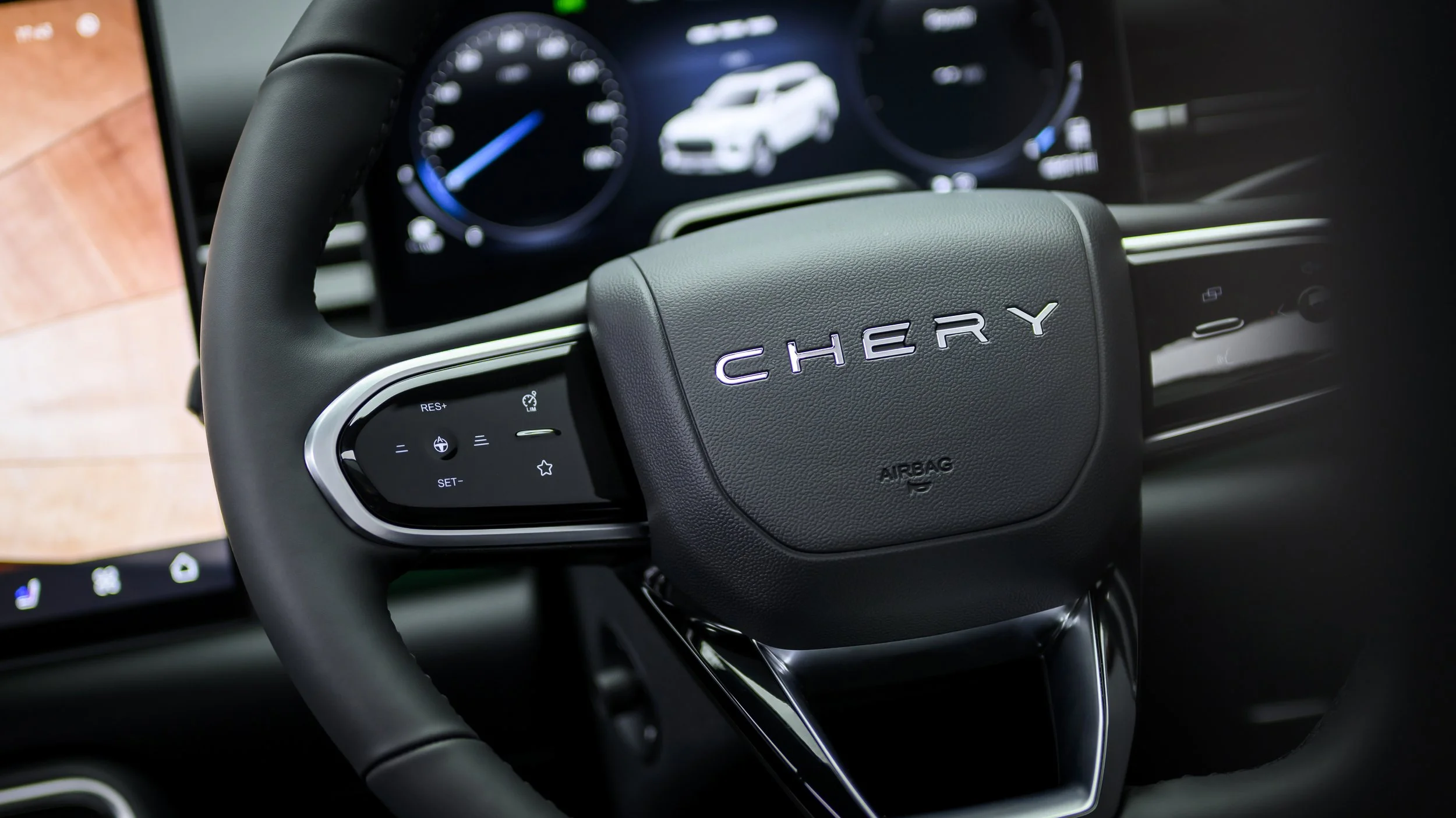 Close-up of a car steering wheel with the brand name 'Chery' in the center, with a digital dashboard showing a white car icon in the background.