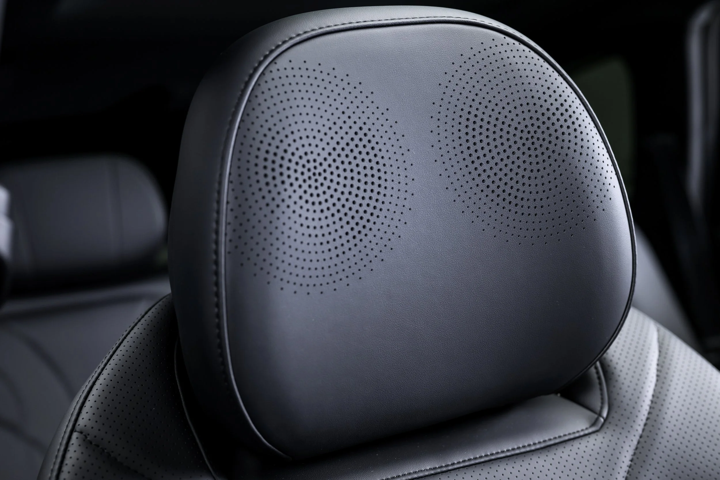 Close-up of a car's headrest with built-in speakers, made of black leather with perforated detailing.