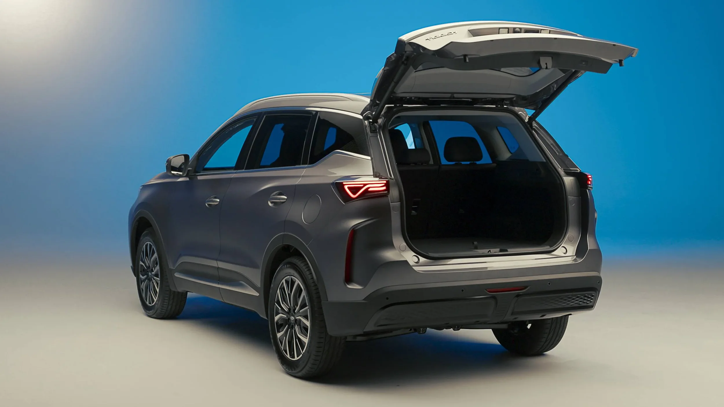 A gray SUV with an open rear hatch showing its interior, set against a plain background.