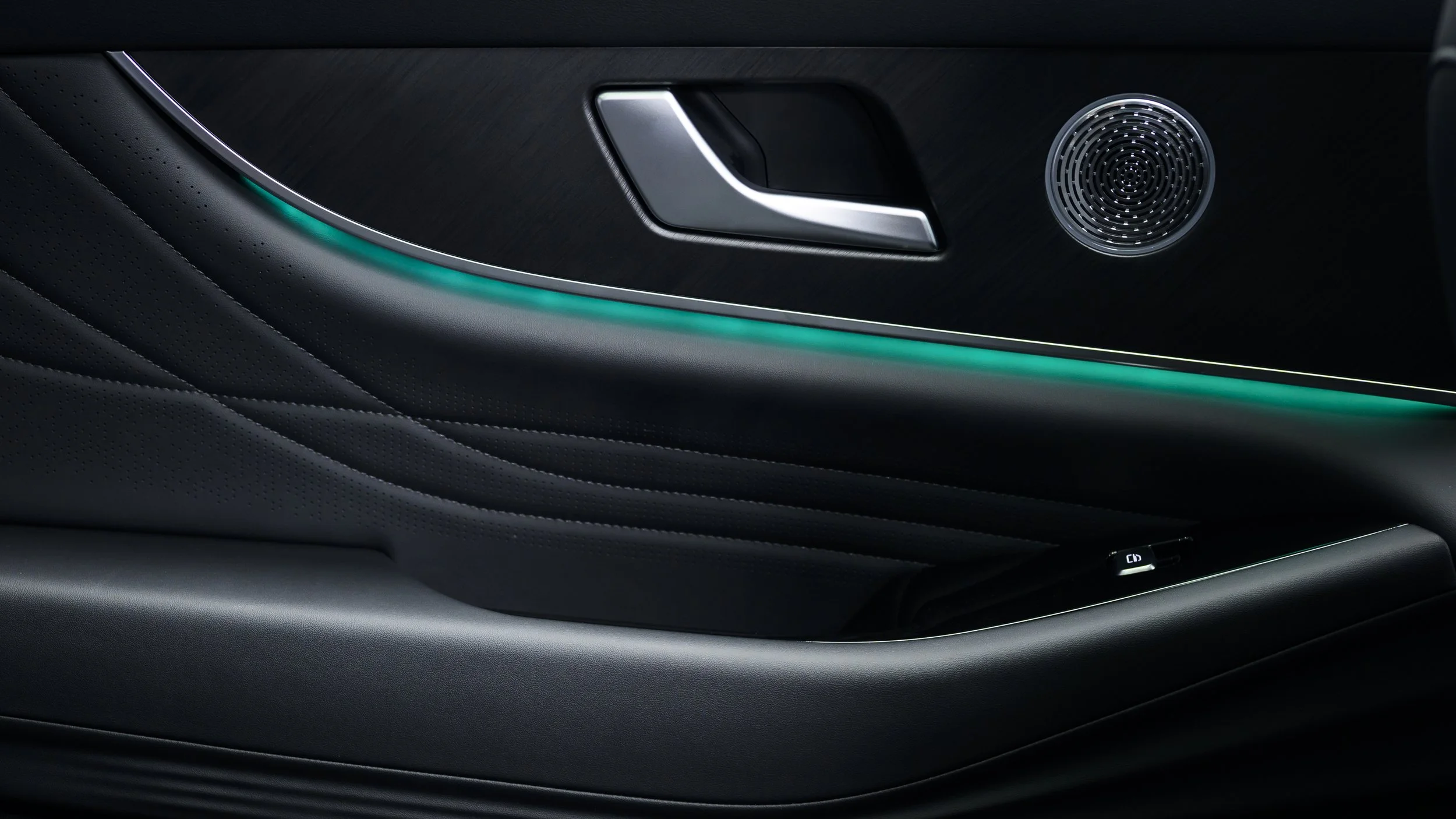 Close-up of a modern car interior door panel with metallic door handle, speaker, and ambient lighting.