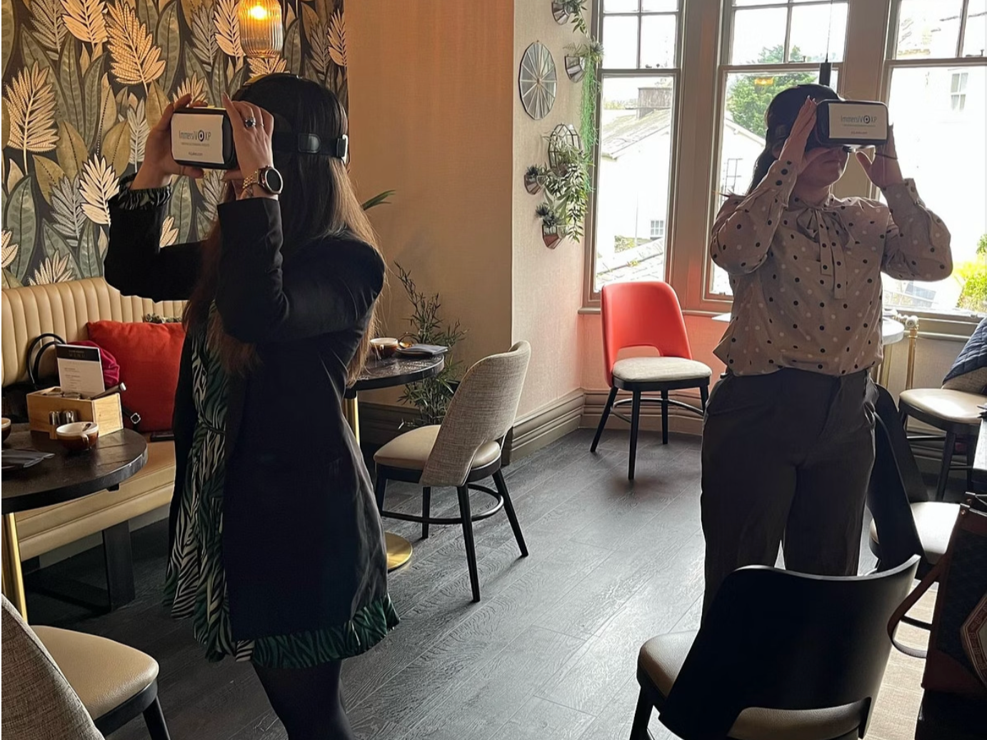Two women trying out the ImmersiV XP Virtual Reality hospitality training in a hotel setting.