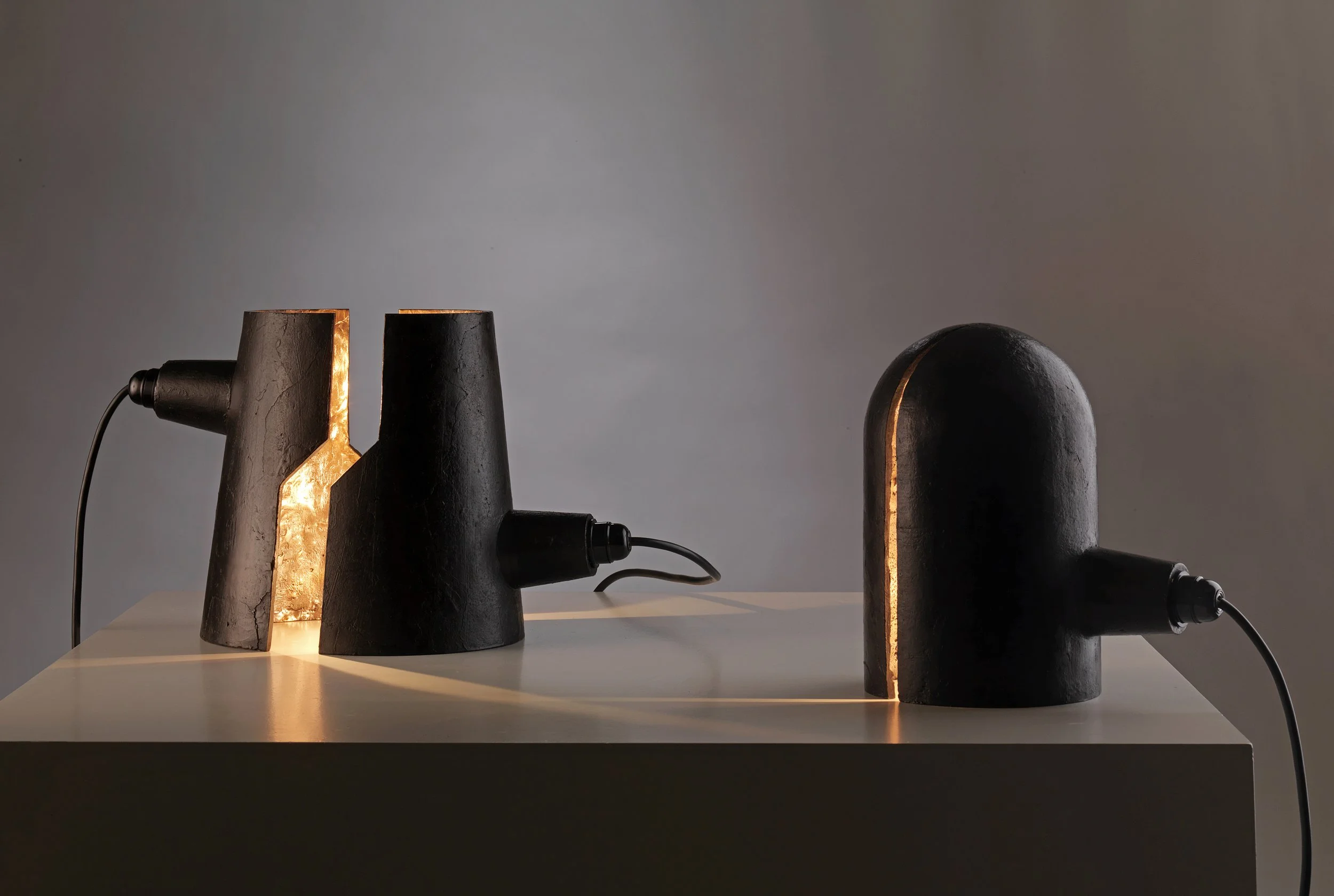 Three black lamps with a cylindrical design and warm interior lighting, placed on a table against a plain background.