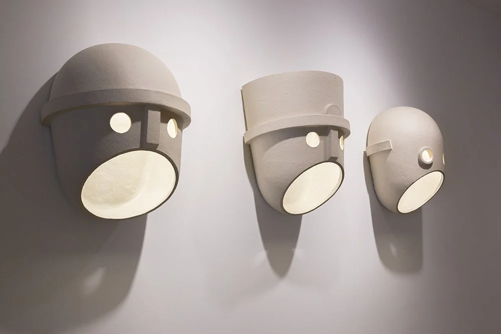 Three minimalist animal face wall sculptures with round eyes and large oval mouths, mounted on a wall.