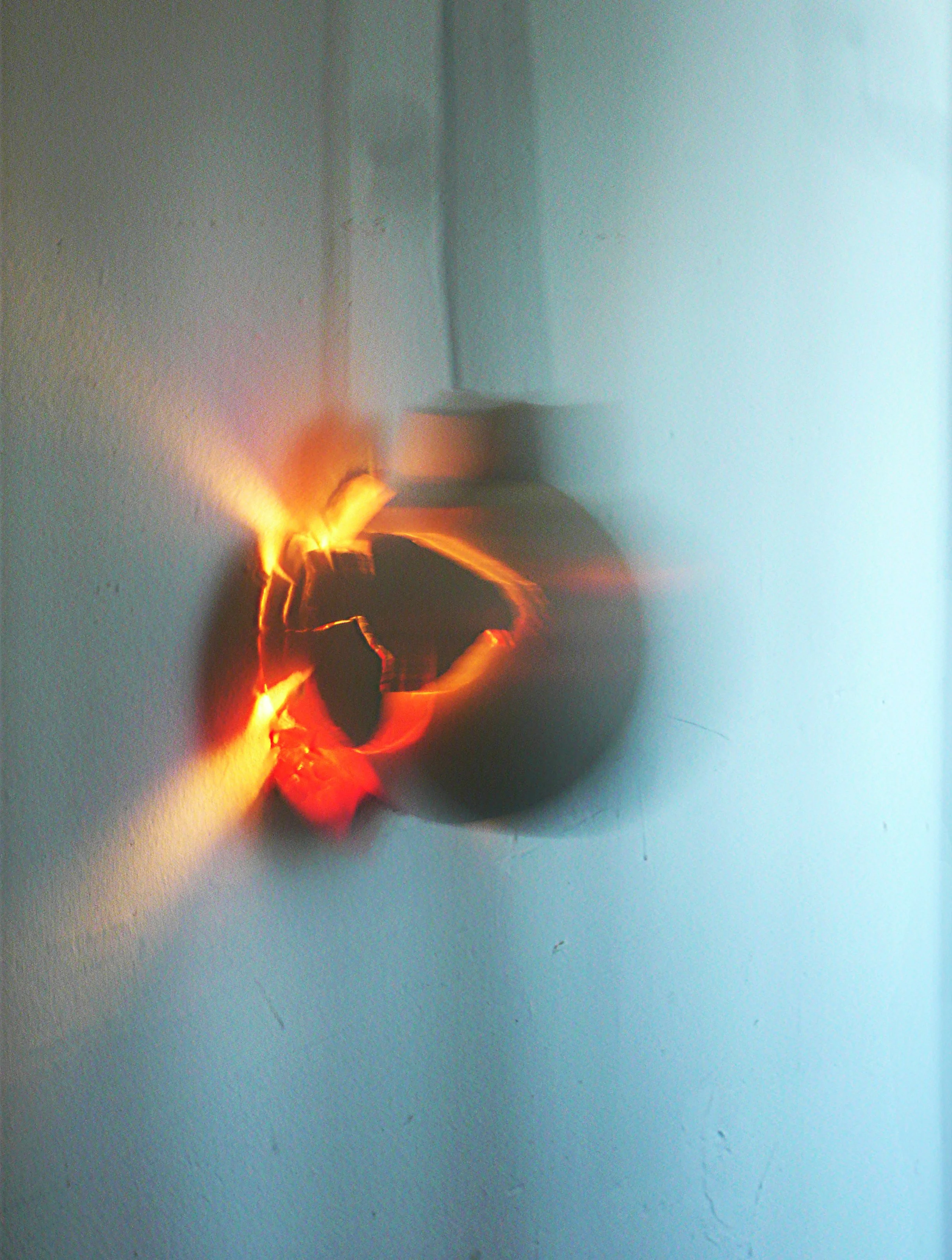 Close-up of a shiny, black electrical outlet with a damaged or burnt area, with visible orange and yellow sparks or flames emerging from it.