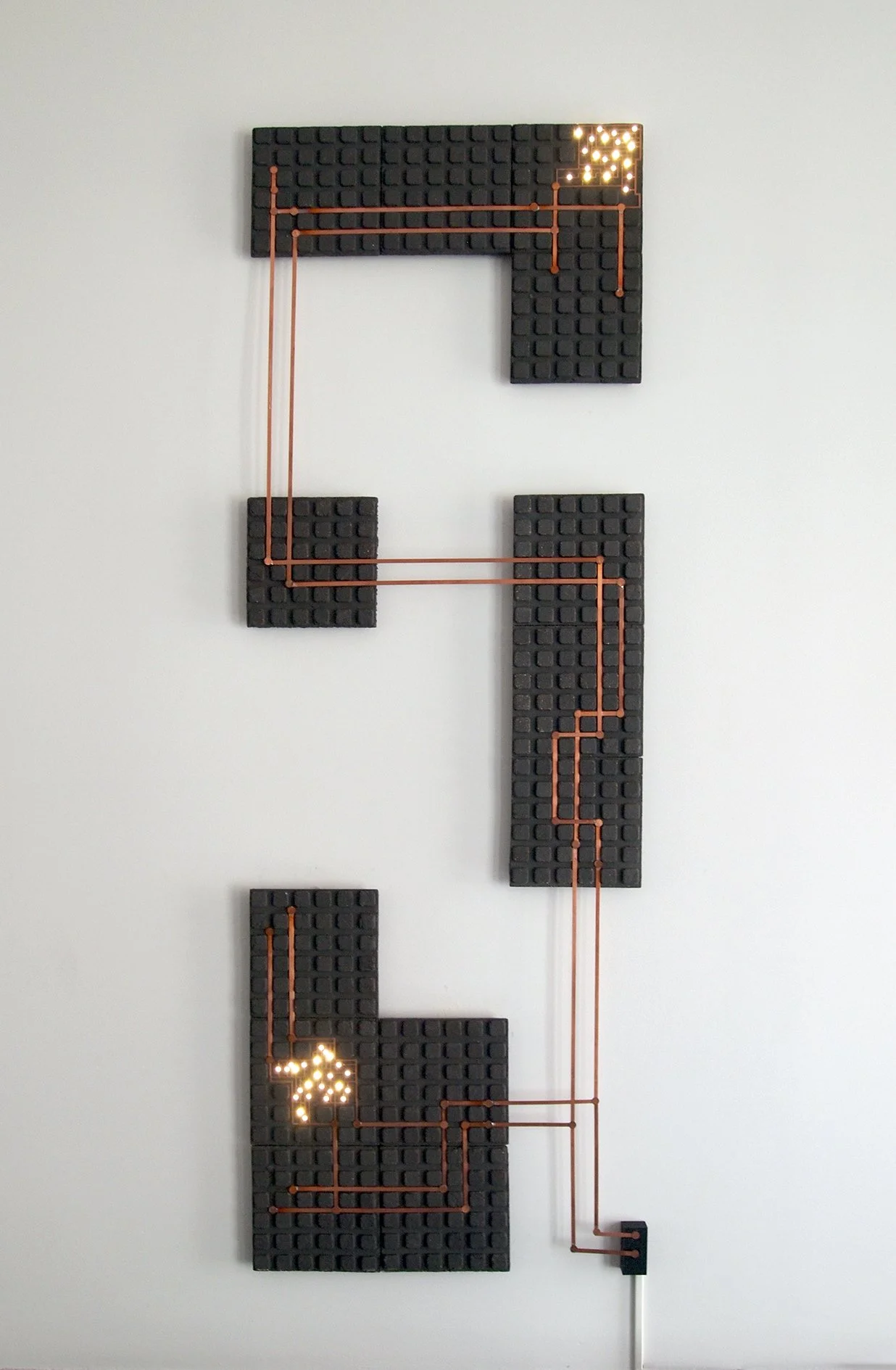 Wall-mounted puzzle with black blocks, copper wires, and illuminated LED arrows in a maze pattern.