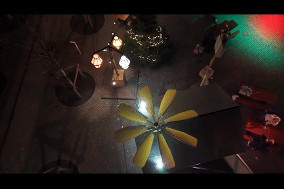 Indoor scene with a ceiling fan, Christmas tree with lights, and various illuminated lamps and decorations.