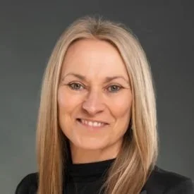 A woman with long blonde hair smiling, wearing a black top, against a plain background.