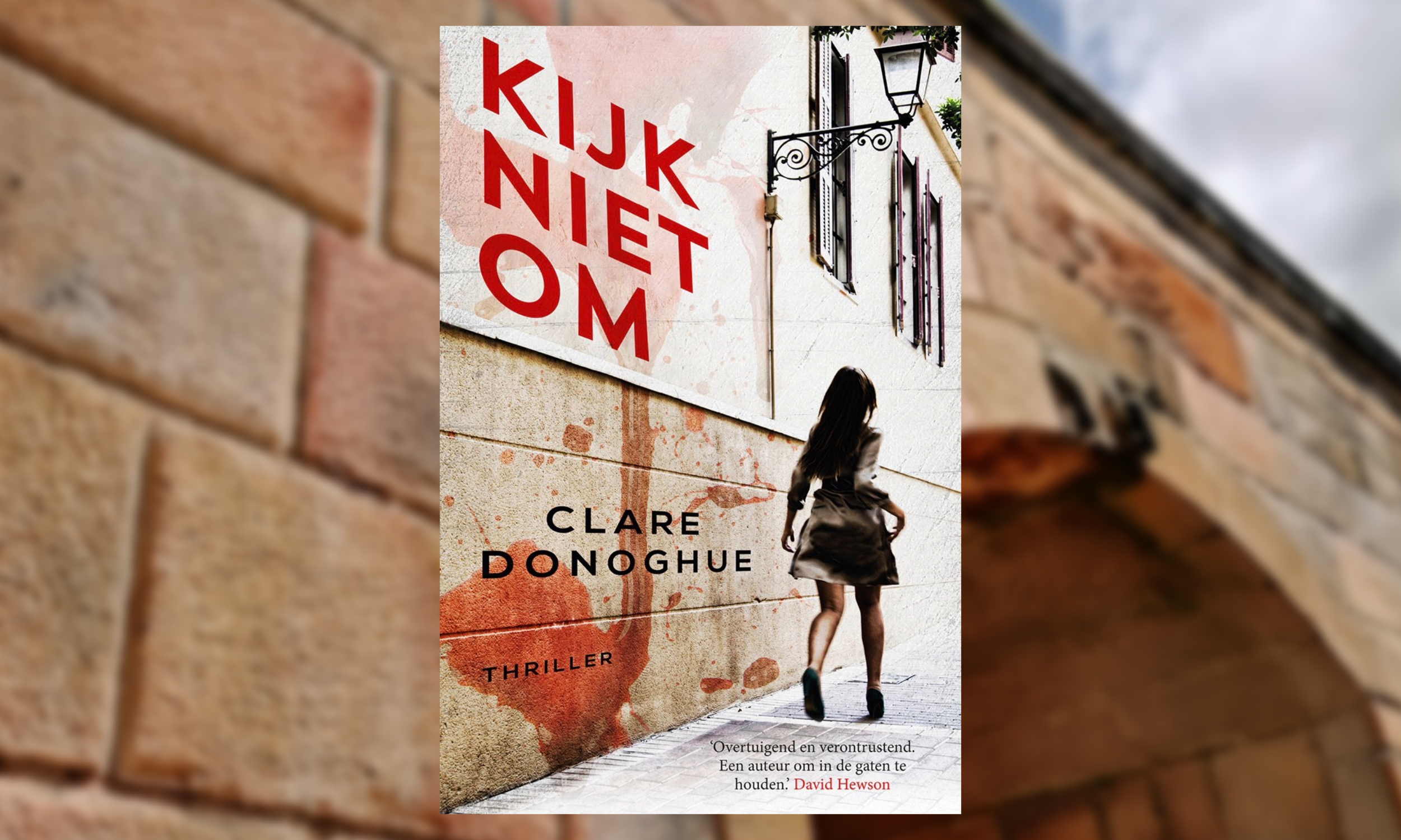 Book cover for 'Kijk Niets Om' by Clare Donoghue featuring a woman walking down a city alley with a white wall, brown bricks, and a large red paint splatter behind her.