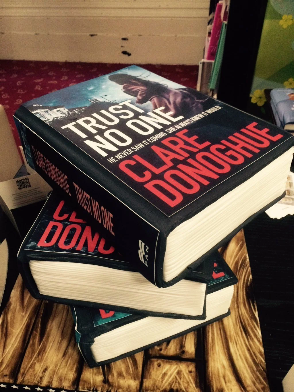 Stack of large paperback books titled 'Trust No One' by Clare Donoghue on a wooden table.