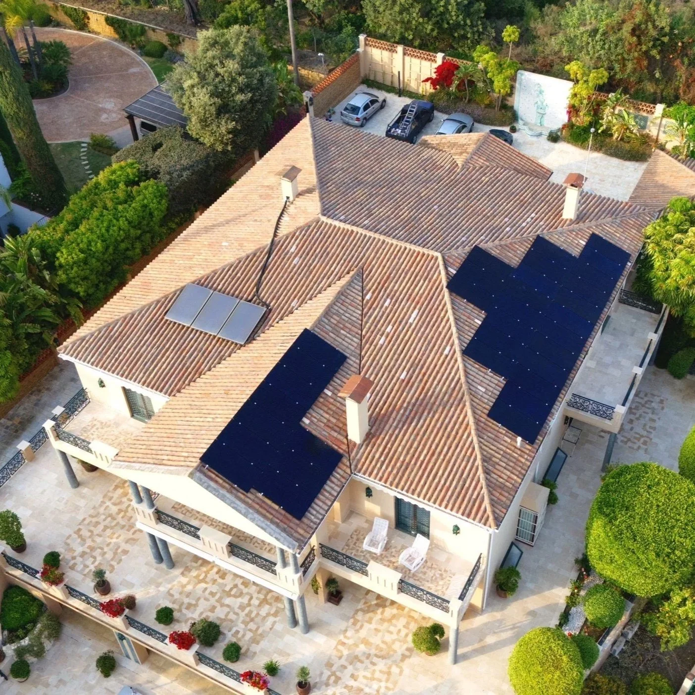 Vista aérea de una casa con varias áreas de terraza, algunos paneles solares en el techo y un jardín con árboles y plantas.