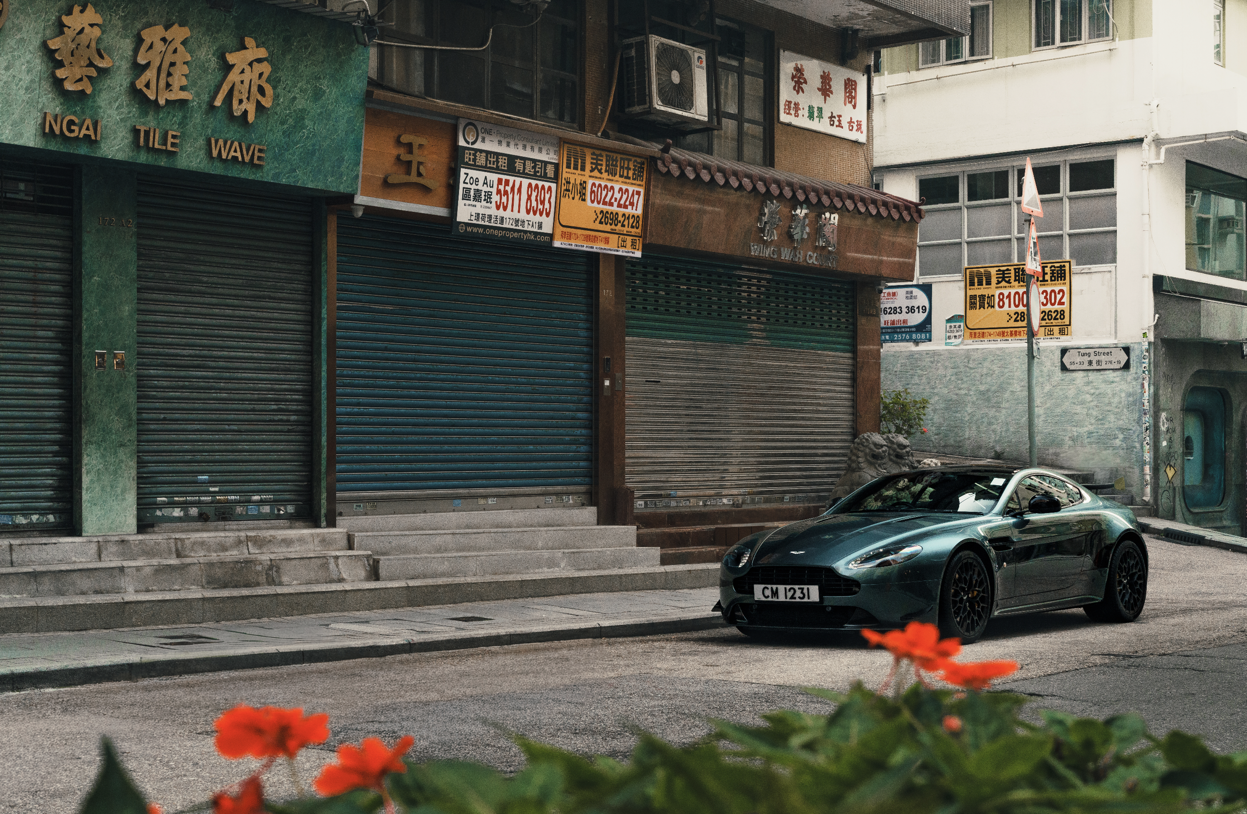 Street scene with closed storefronts, parked luxury car, and colorful flowers in the foreground.