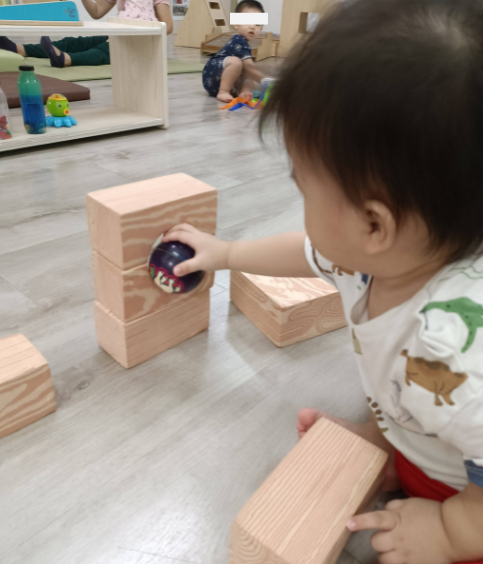 Infant attempting to place a ball through an opening in a block structure.