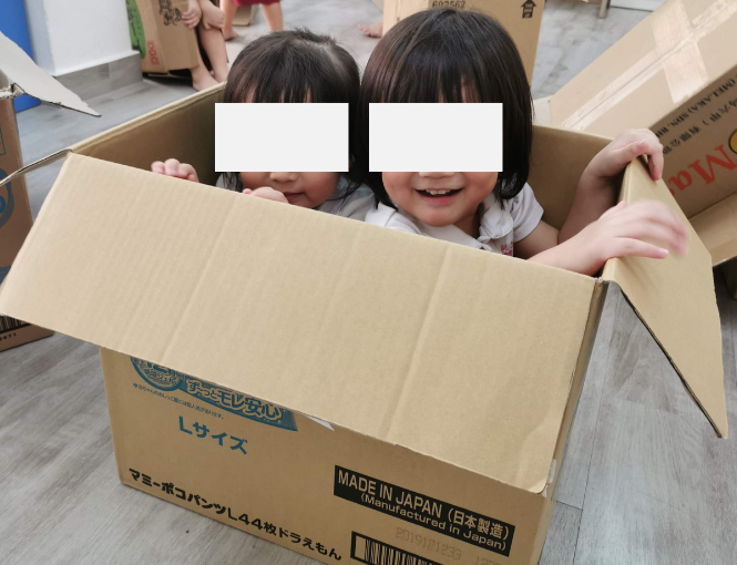 Two young children sitting inside a large cardboard box during imaginative play.