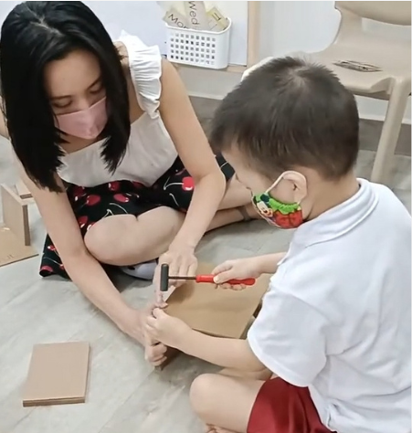 Hermes Lu guiding a child as they learn to use a hammer and nail safely.