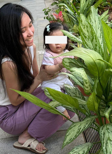 Young infant reaching towards garden leaves while being carried outdoors by Hermes Lu.