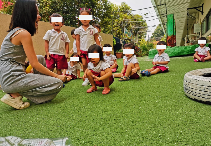 Hermes Lu with a group of toddlers outdoors at a gentle slope during a cause-and-effect exploration activity.