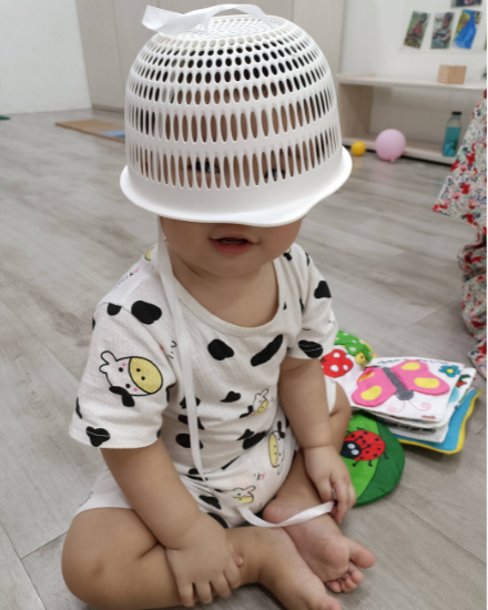 Infant playing peekaboo with a small basket covering their eyes.