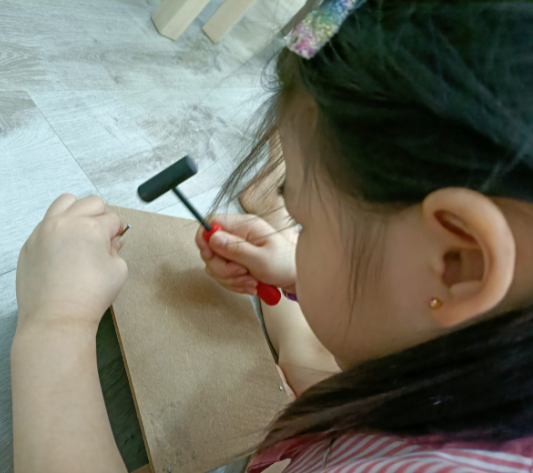 Young child positioning a nail and hammer while learning basic woodworking skills.